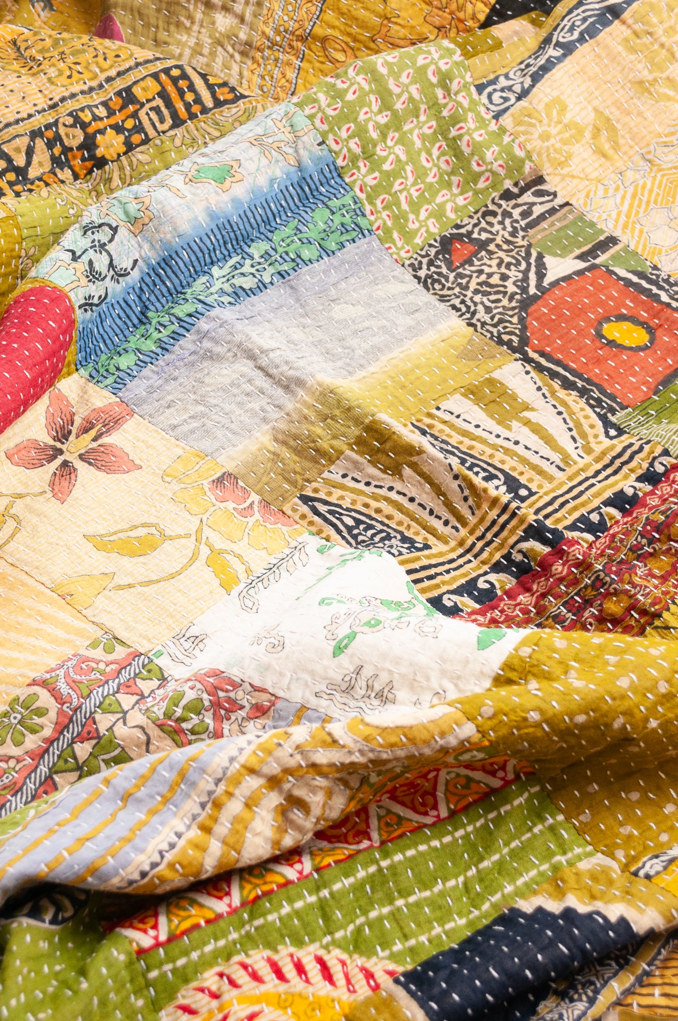 Vintage patchwork kantha quilt in multiple prints with green base.