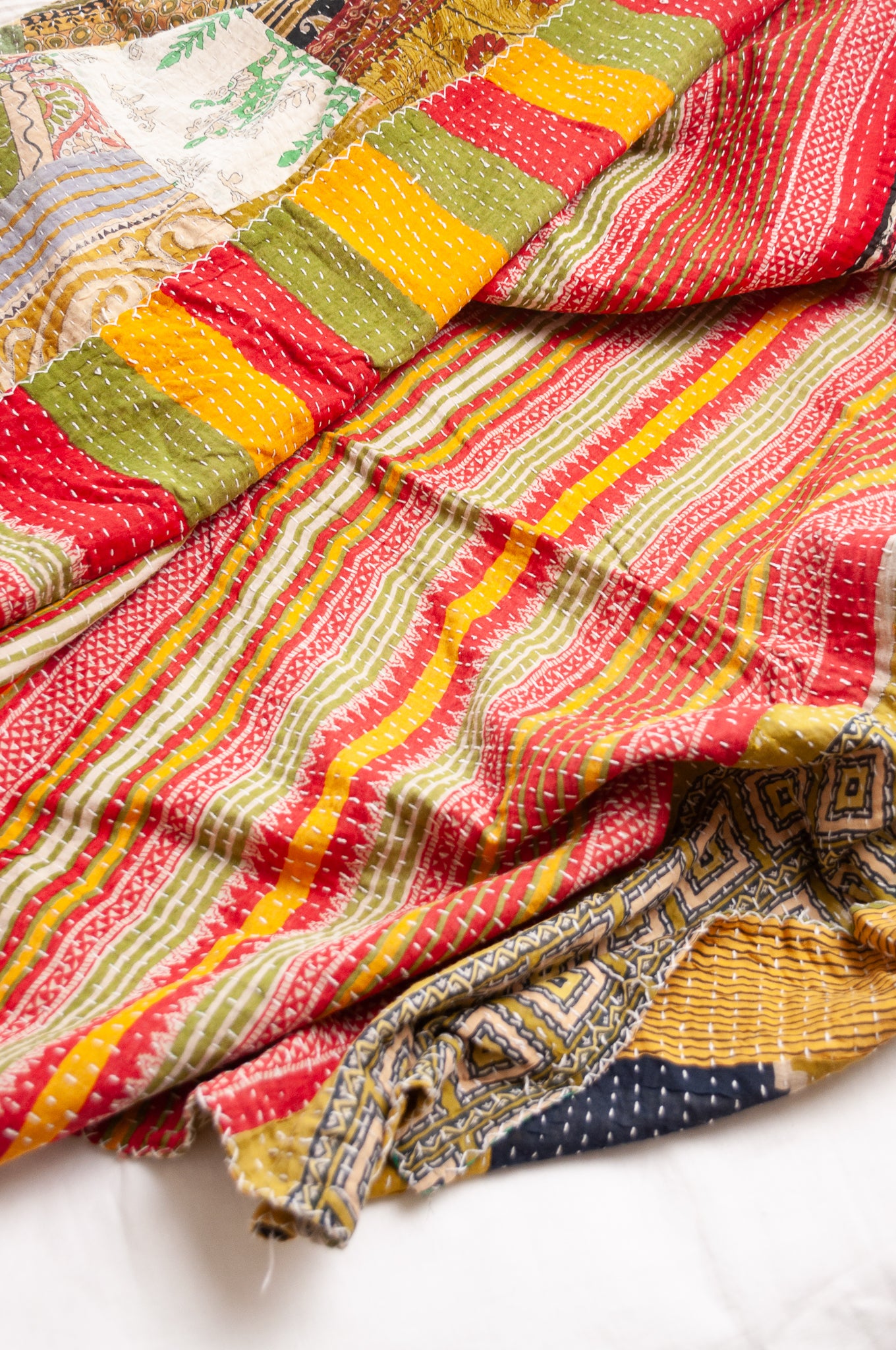 Vintage patchwork kantha quilt in multiple prints with green base.