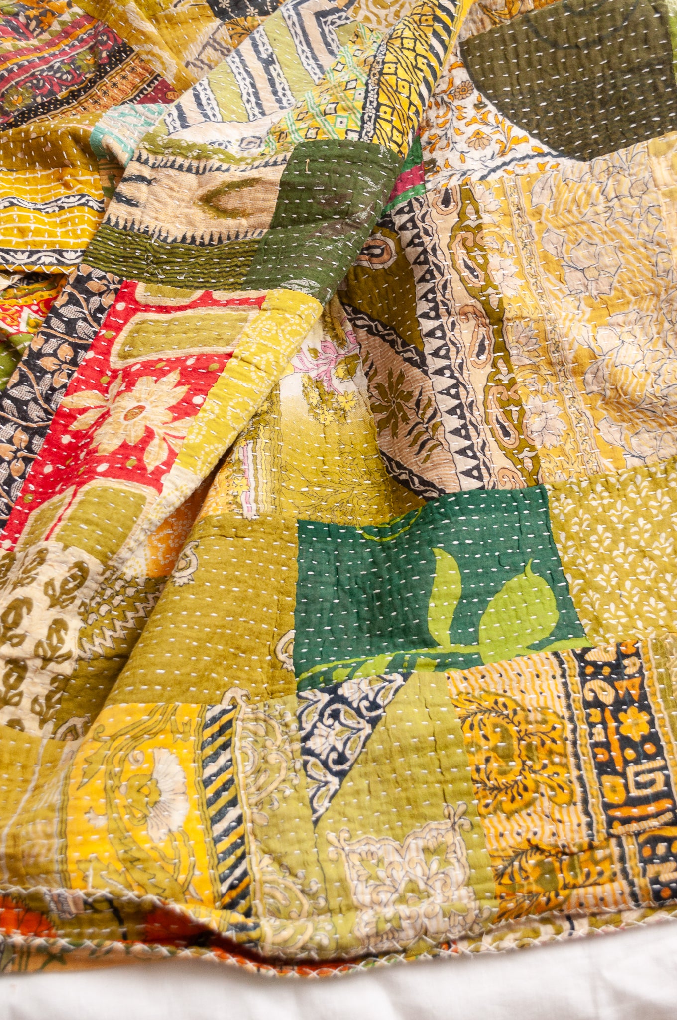 Vintage patchwork kantha quilt in multiple prints with green base.