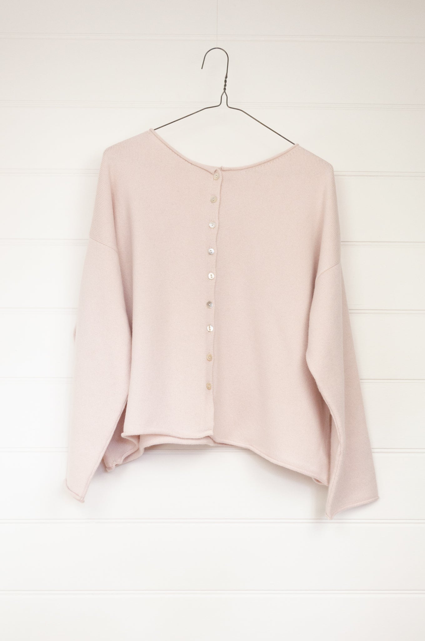 A reversible ecru cashmere cardigan hanging on a hanger against a white background, showing both the front and back sides with shell buttons.