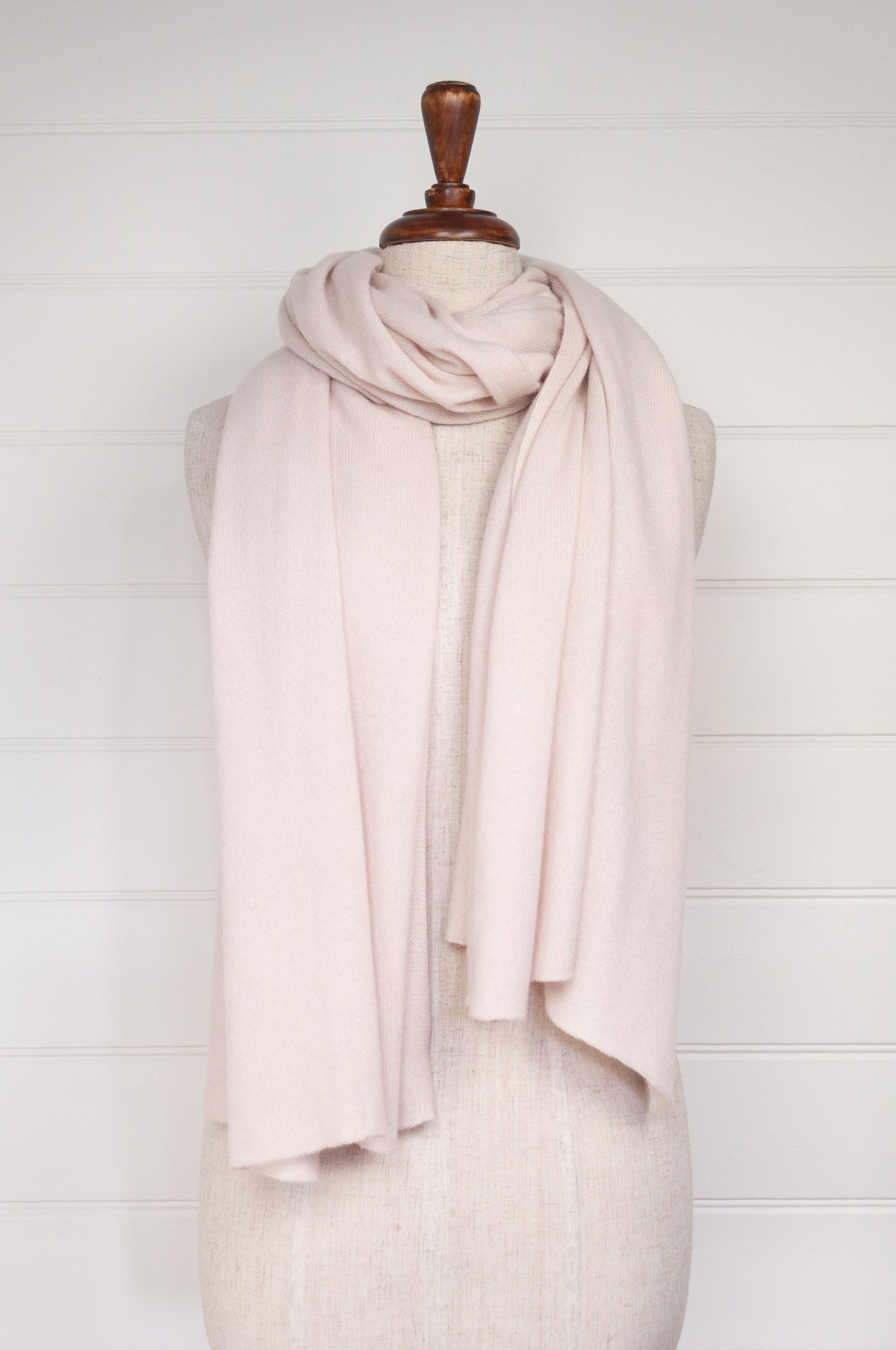 An ecru-colored cashmere scarf draped on a mannequin against a white background, showcasing a lightweight and oversized design.