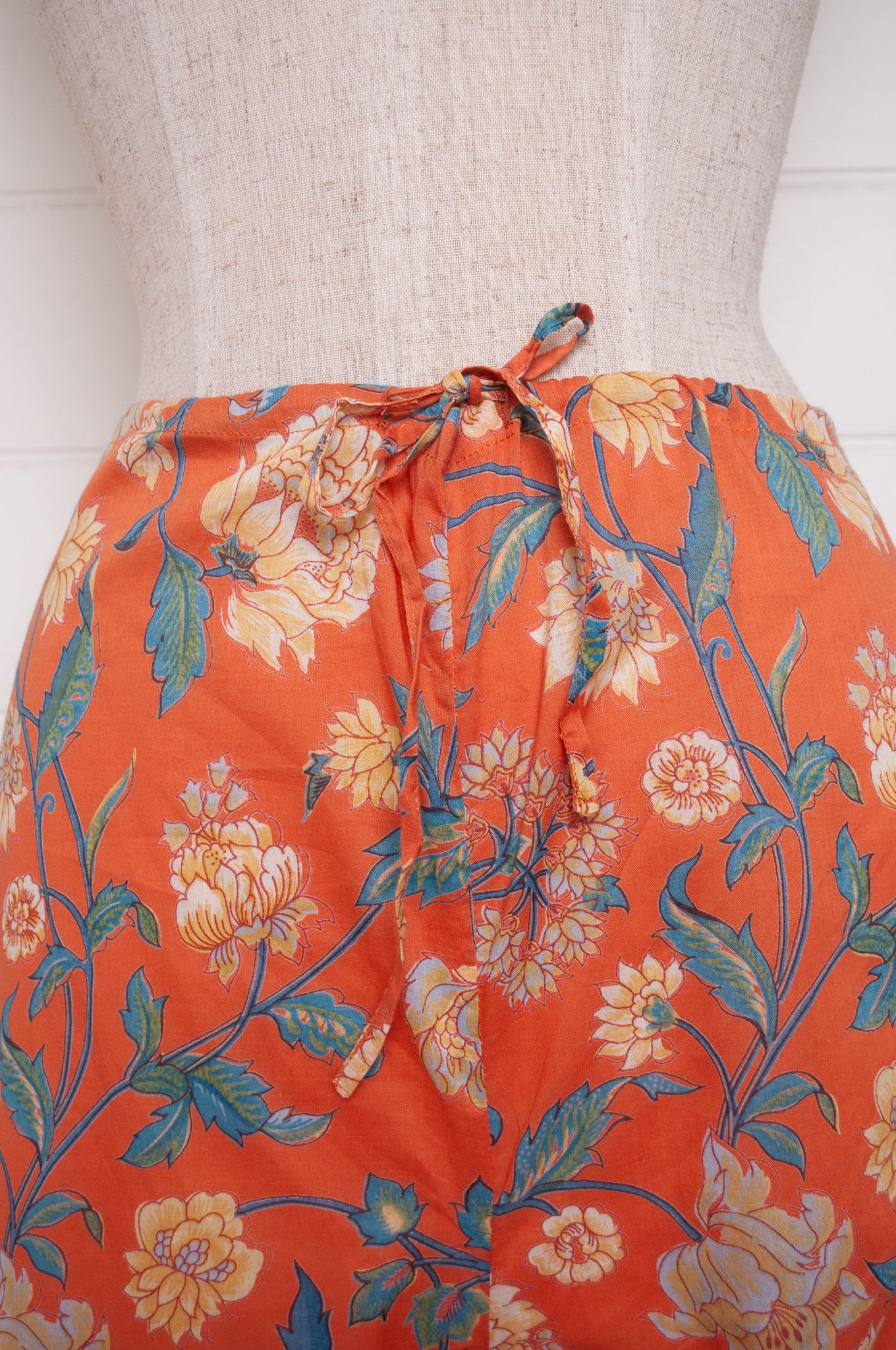 Juniper Hearth pyjama set in Kashmir saffrron, vanilla flowers on orange background.
