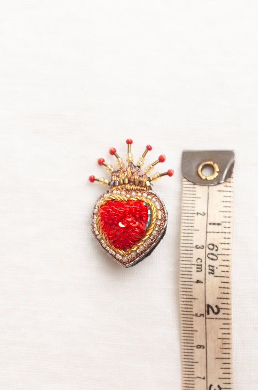 Trovelore Queen of Hearts hand beadedheart-shaped brooch featuring a vibrant red central heart, surrounded by a gold and silver beaded border, topped with a small gold crown adorned with red beads.