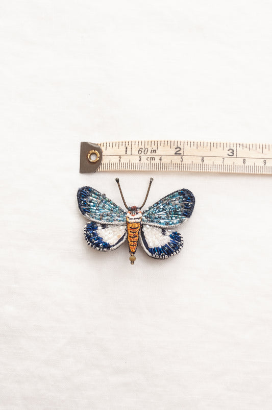 Trovelore Neochera moth hand beaded brooch, detailed butterfly-shaped brooch with iridescent blue and white wings, a metallic gold body, and delicate antennae.