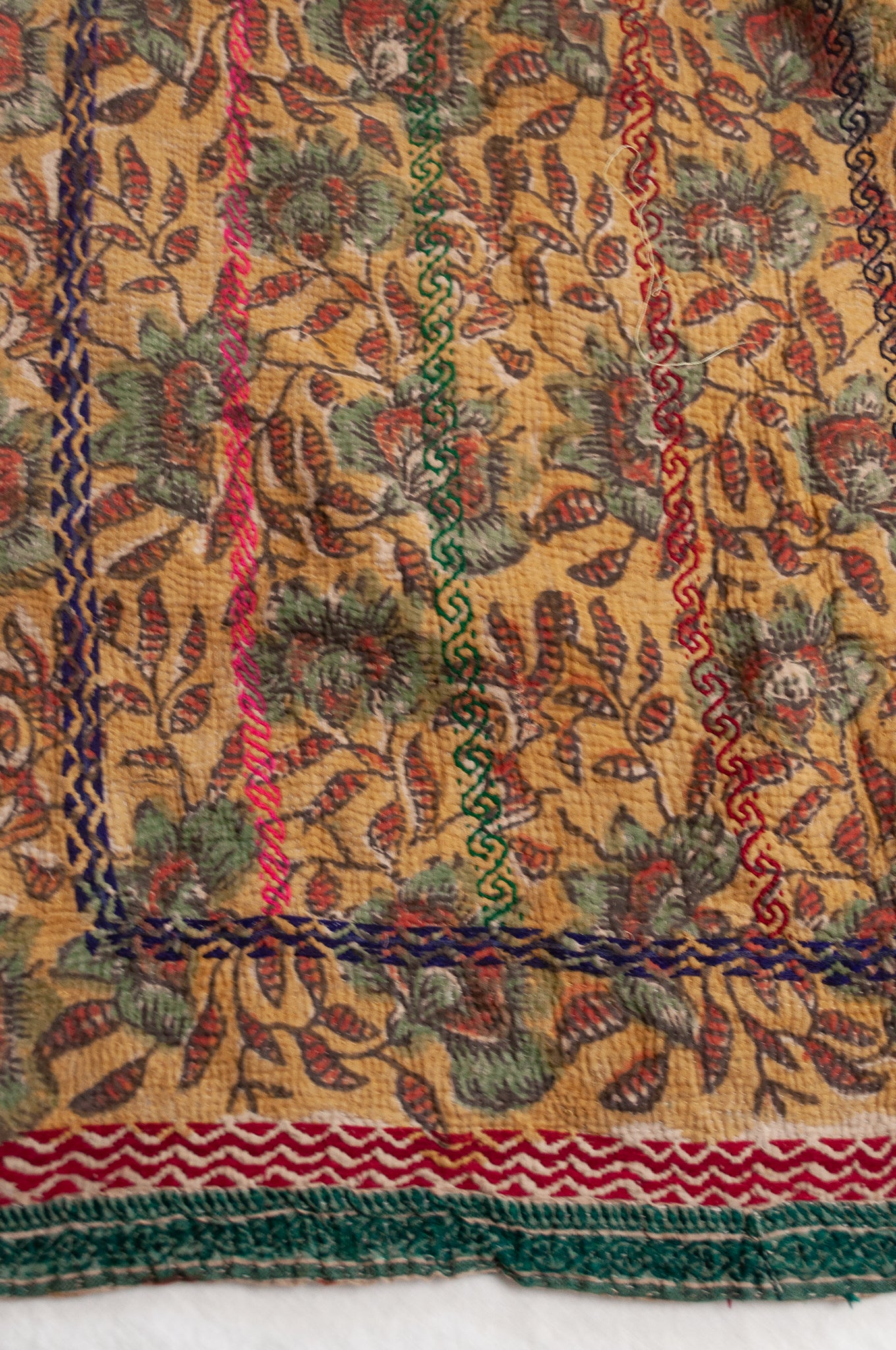 Vintage bagru blockprinted kantha quilt, floral design in rust red and sage green on a mustard yellow background, with red, blue and green traditional decorative embroidery