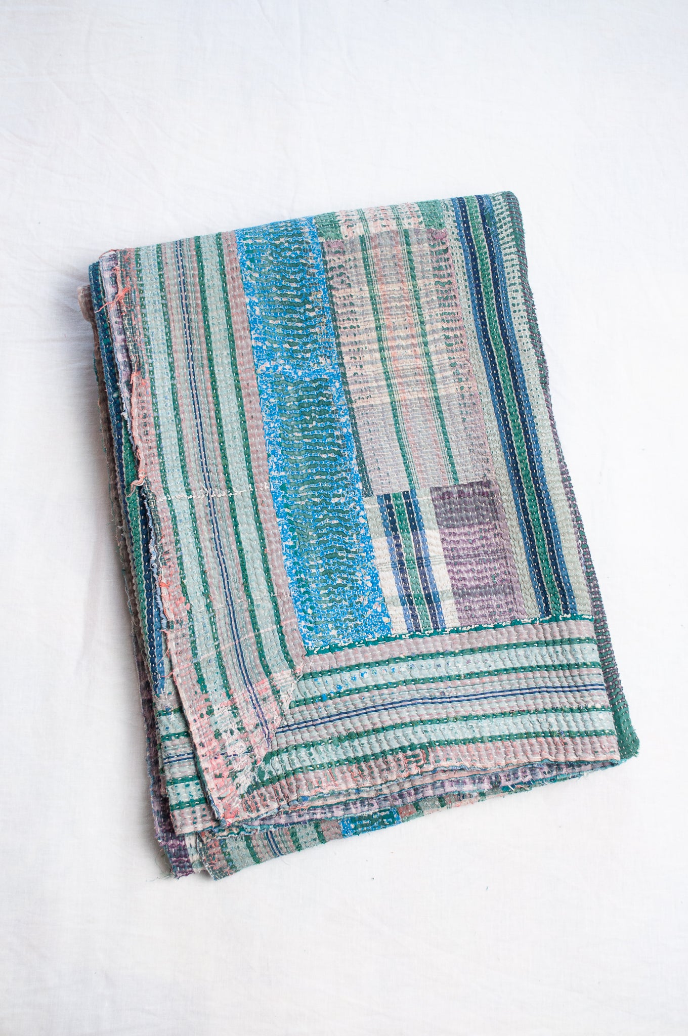Striped kantha quilt, with checks and patches in greens and blues with highlights of pink.