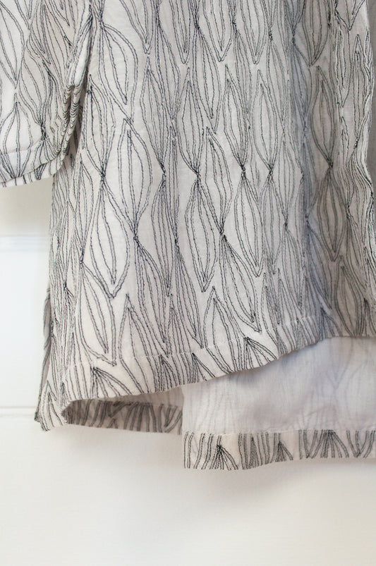 Neeru Kumar Pyke jacket in white cotton silk, featuring embroidered leaf motif. Long A-line kimono style with long sleeves and side slits at hem.