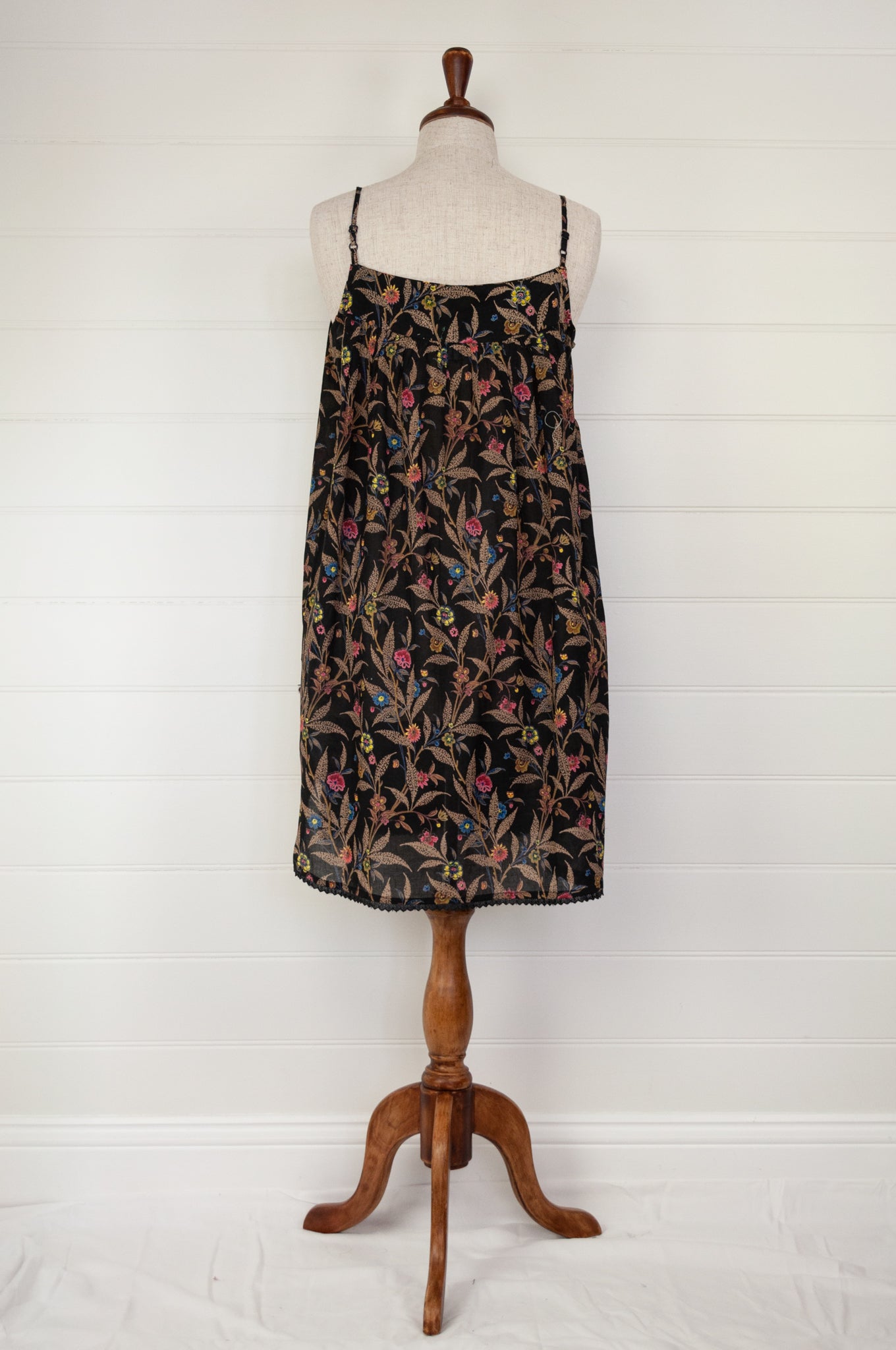 Ethically made pure cotton voile summer nightdress with adjustable straps and pintucked yoke, this nightie is in a wildflower print on black with broderie edging (back view).