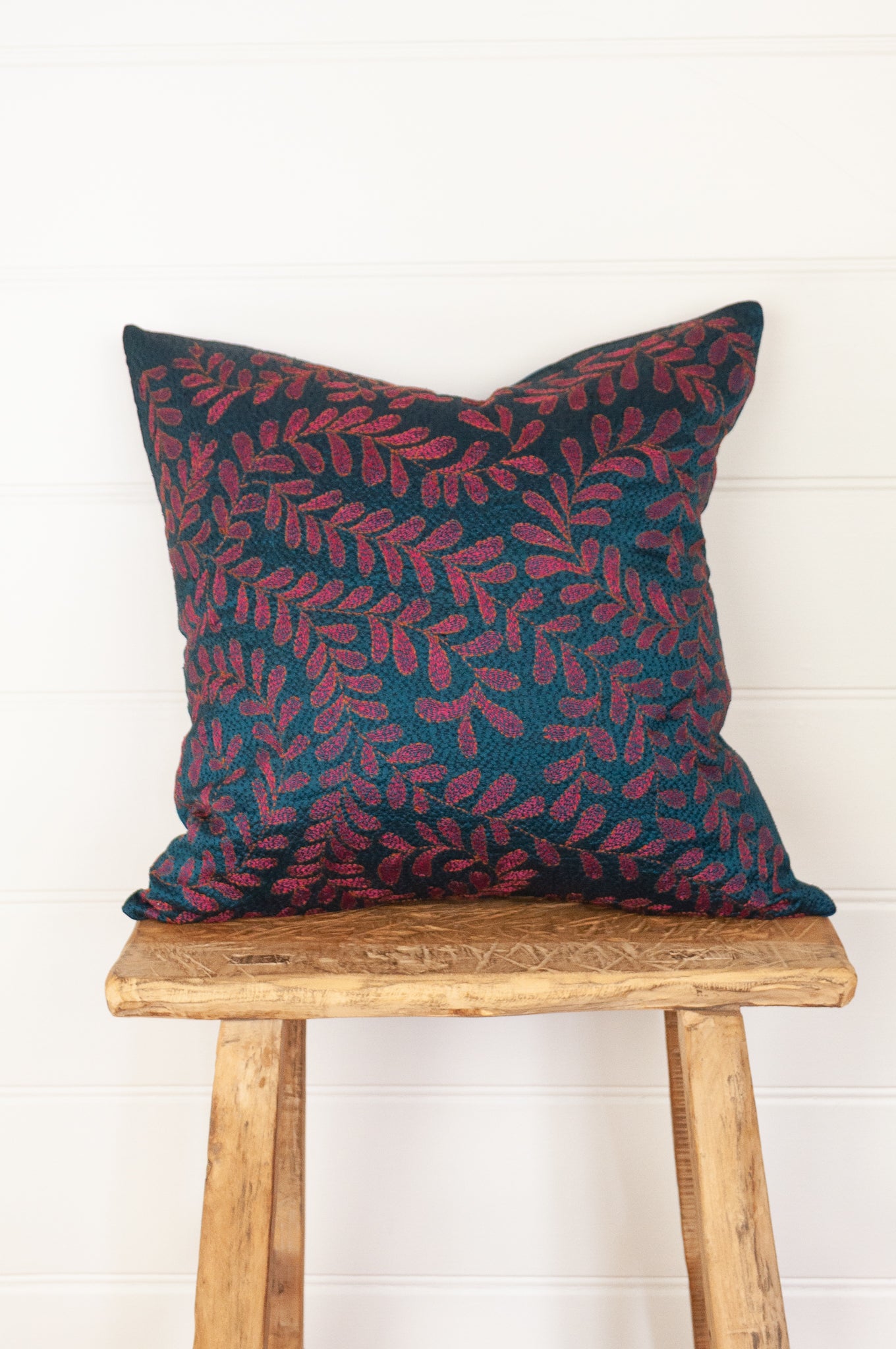BKantha stitched on vintage silk, this square cushion features an allover tracery of vine leaves in cherry red on a black stitched teal blue background.