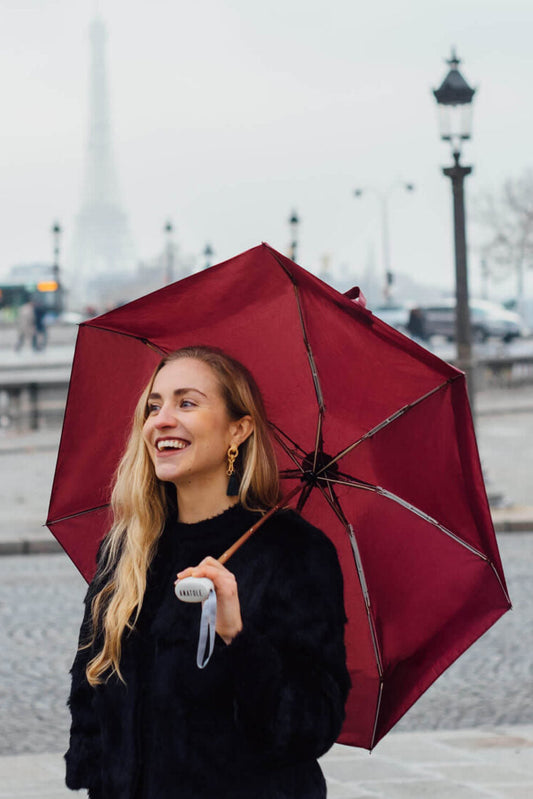 Woman holding an Anatole Germain burgundy maroon micro umbrella in an urban setting