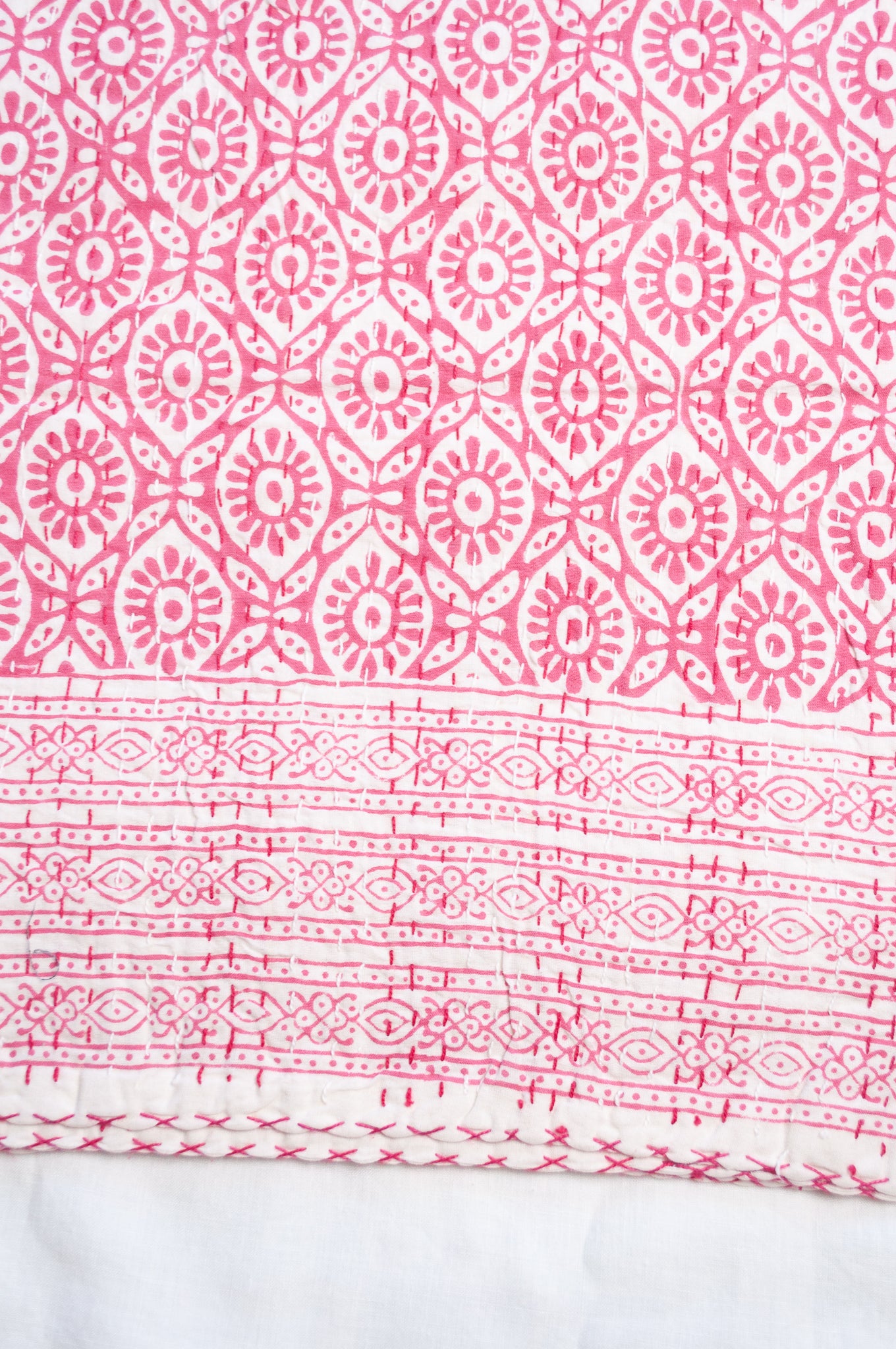 Cotton kantha quilt with an abstract floral design in pink on white.