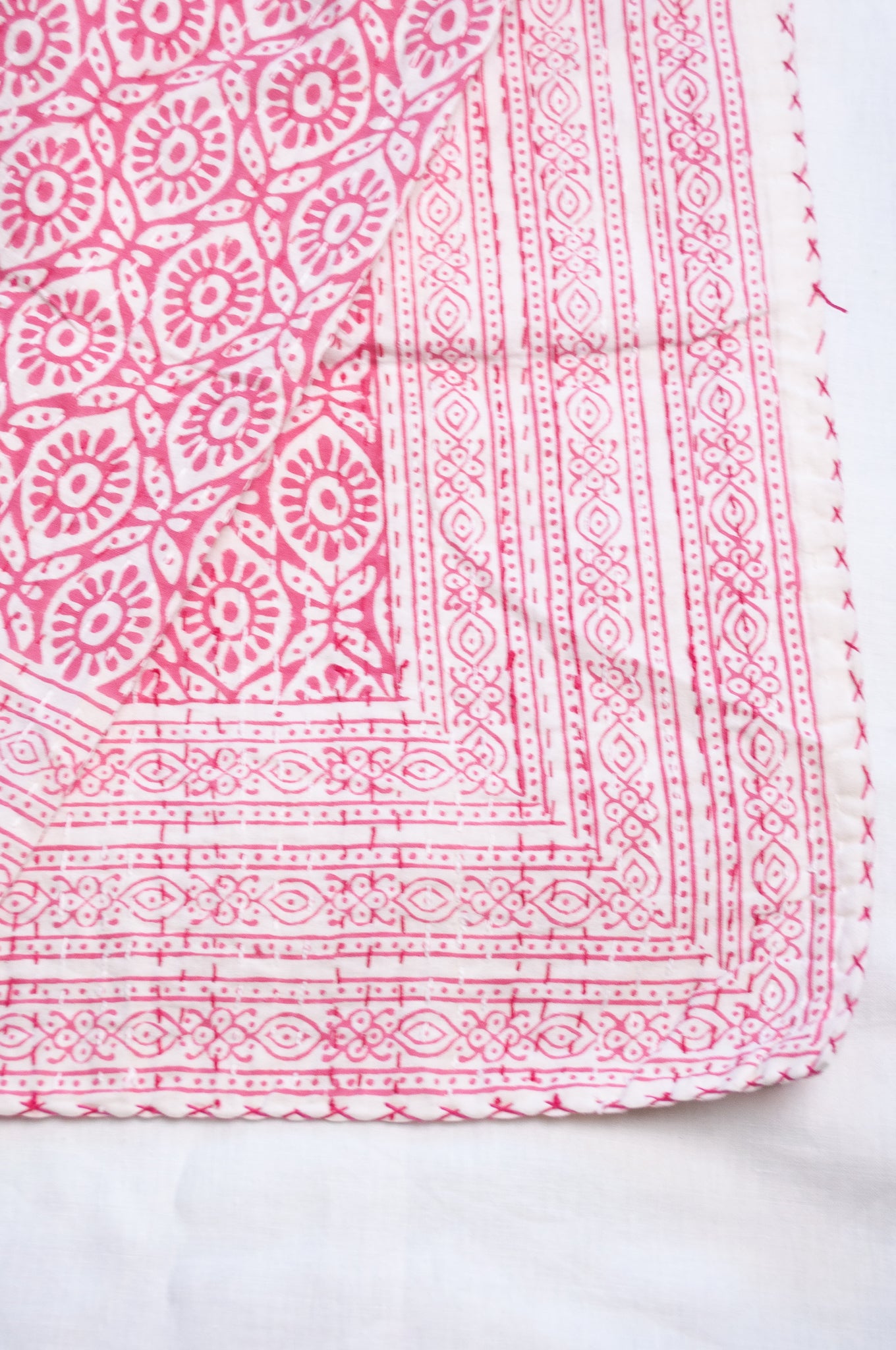 Cotton kantha quilt with an abstract floral design in pink on white.