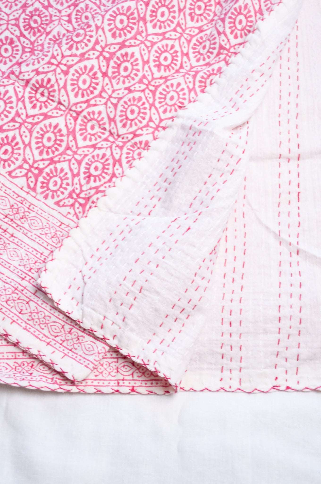 Cotton kantha quilt with an abstract floral design in pink on white.