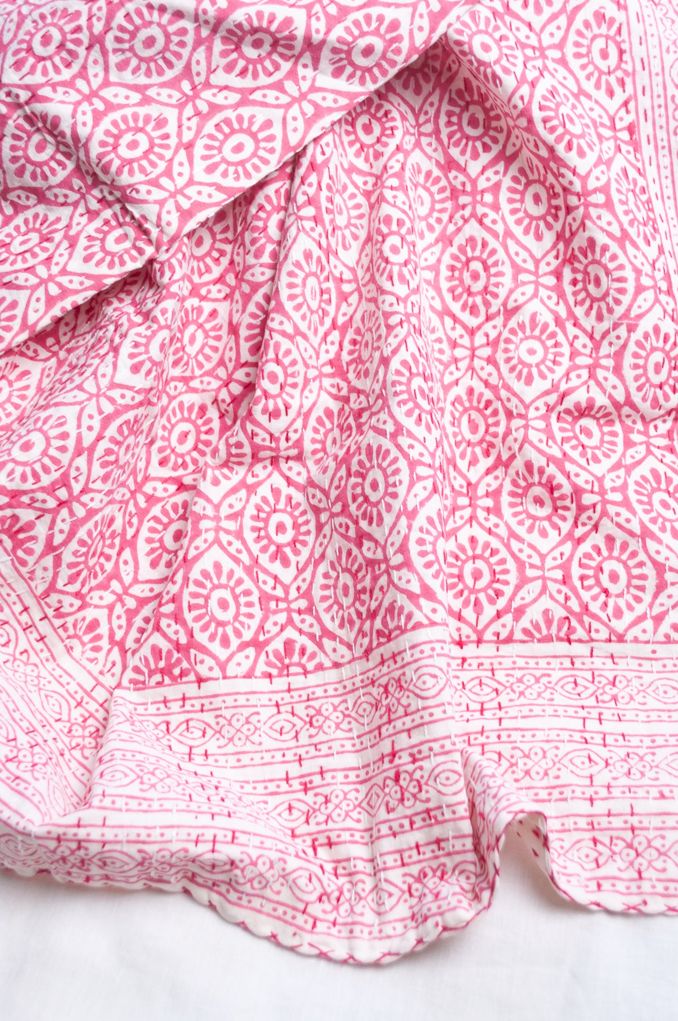 Cotton kantha quilt with an abstract floral design in pink on white.