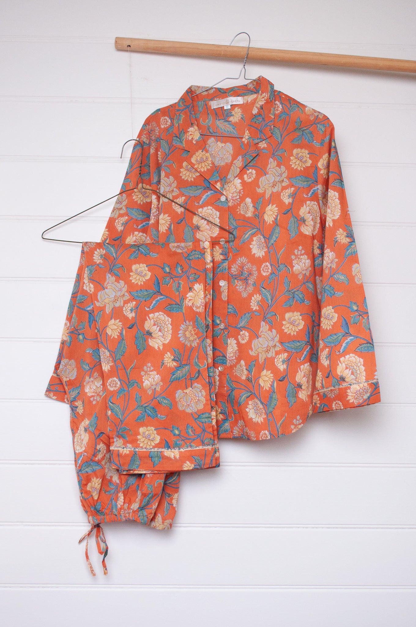 Juniper Hearth pyjama set in Kashmir saffrron, vanilla flowers on orange background.