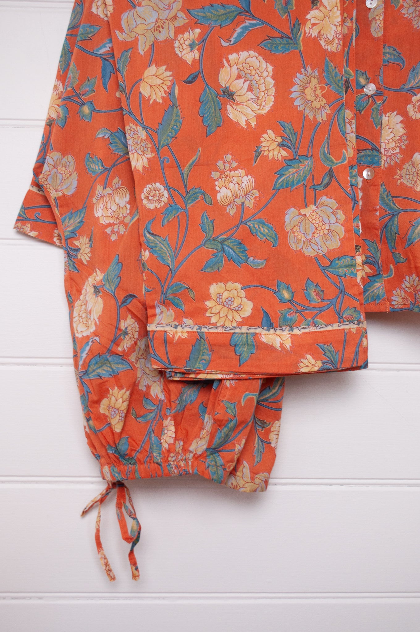 Juniper Hearth pyjama set in Kashmir saffrron, vanilla flowers on orange background.