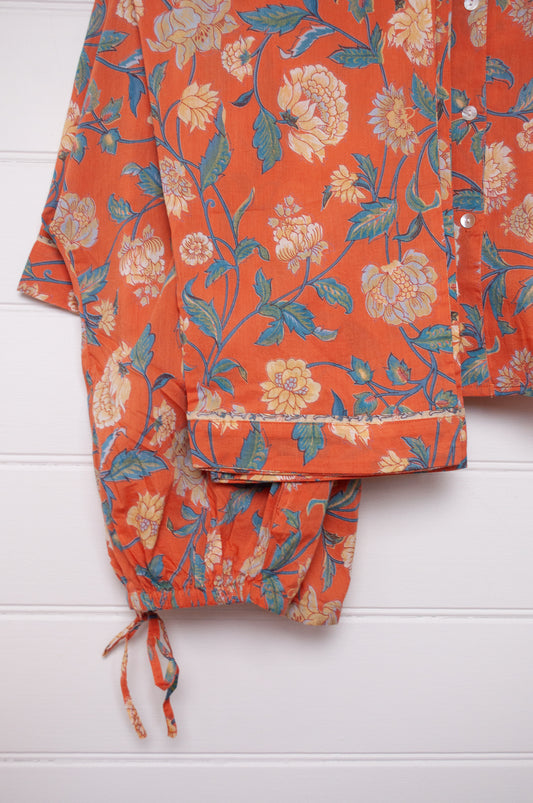 Juniper Hearth pyjama set in Kashmir saffrron, vanilla flowers on orange background.