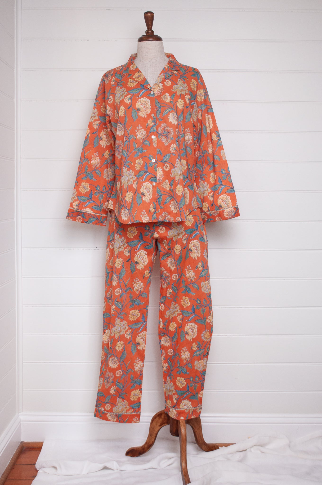 Juniper Hearth pyjama set in Kashmir saffrron, vanilla flowers on orange background.