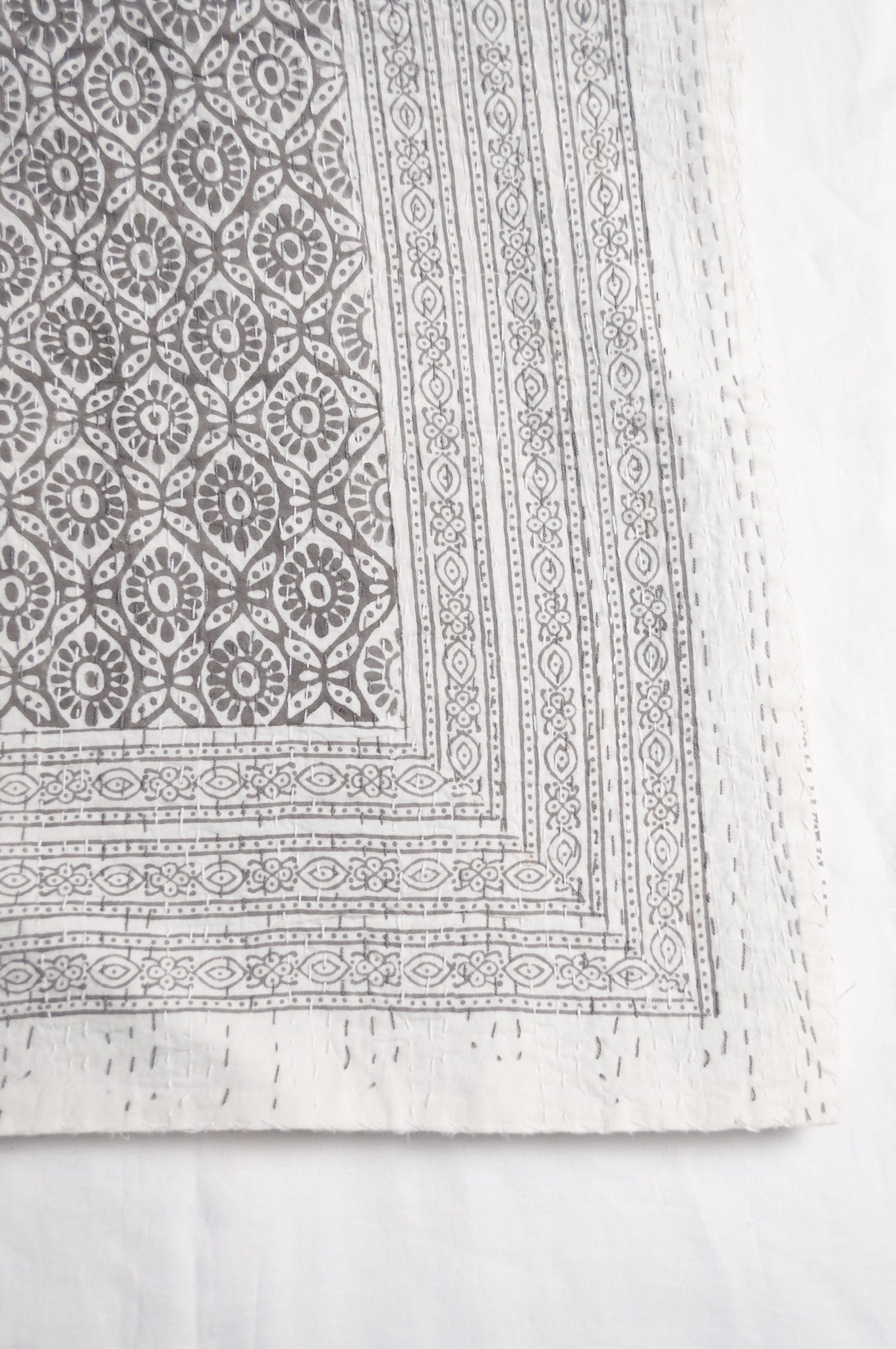 Cotton kantha quilt with an abstract floral design in silver grey on white.