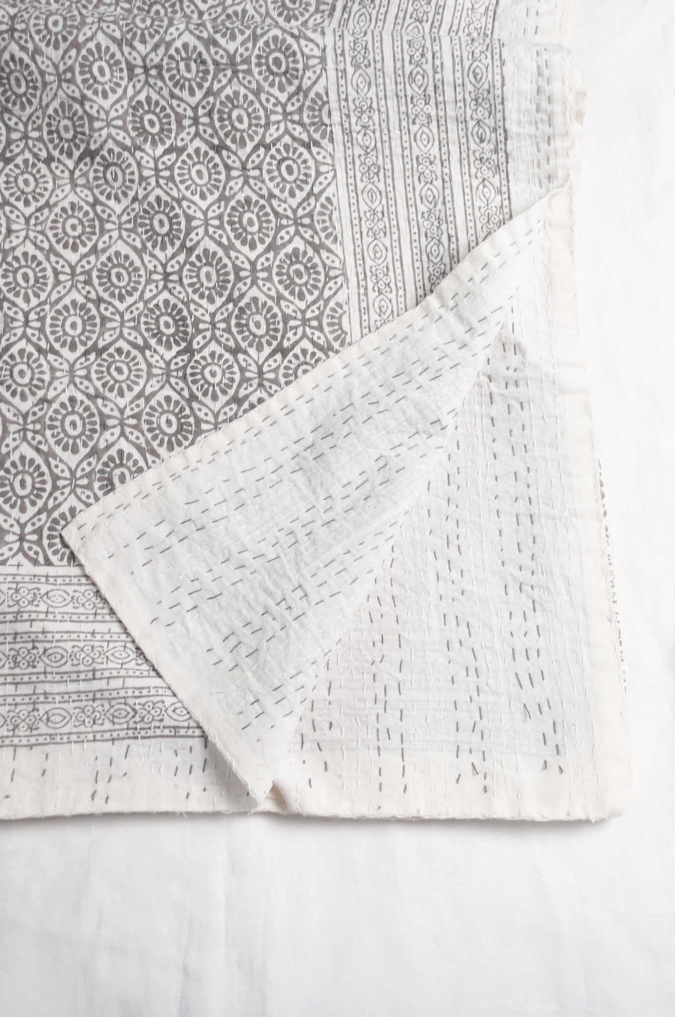 Cotton kantha quilt with an abstract floral design in silver grey on white.