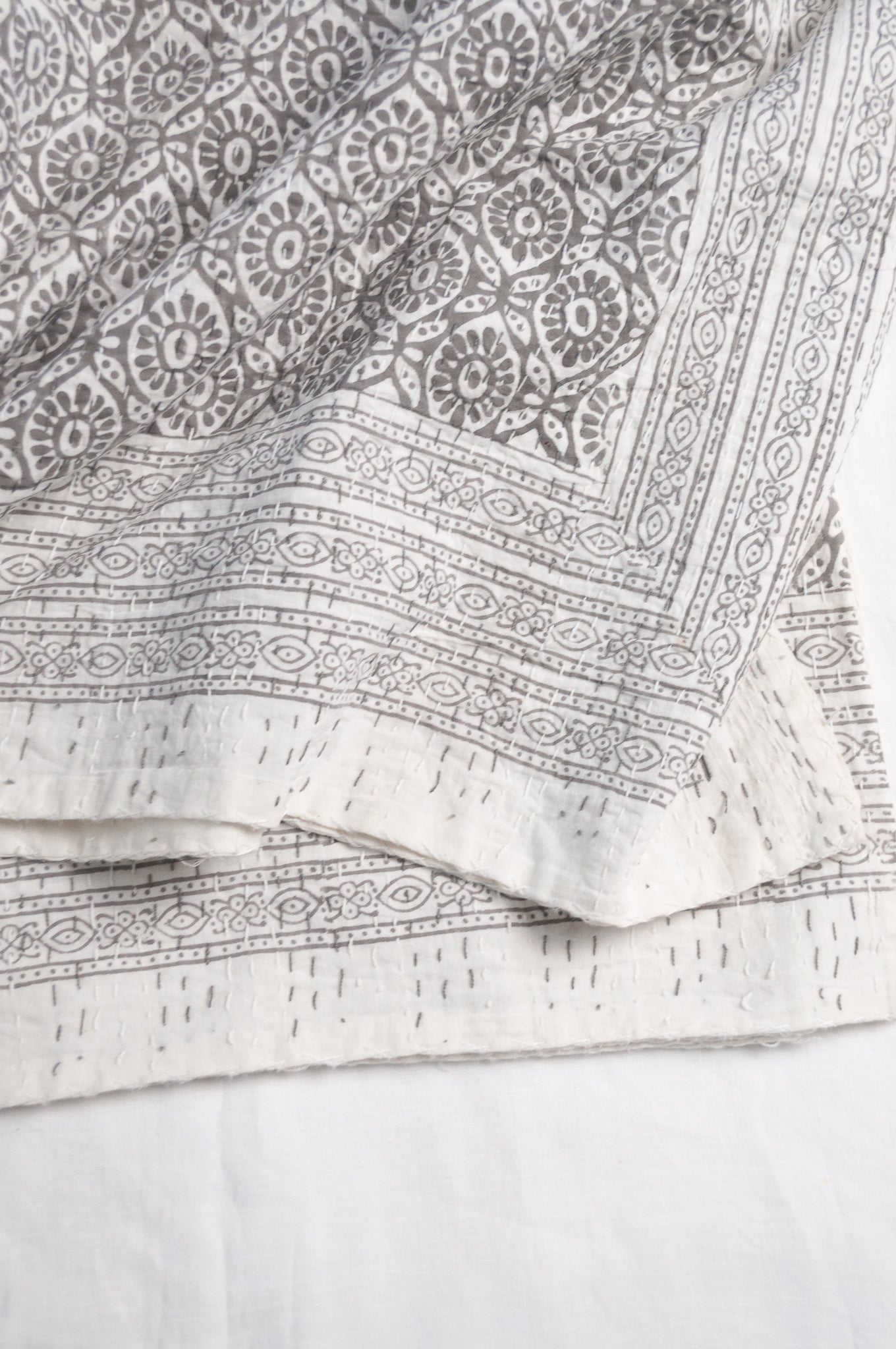 Cotton kantha quilt with an abstract floral design in silver grey on white.