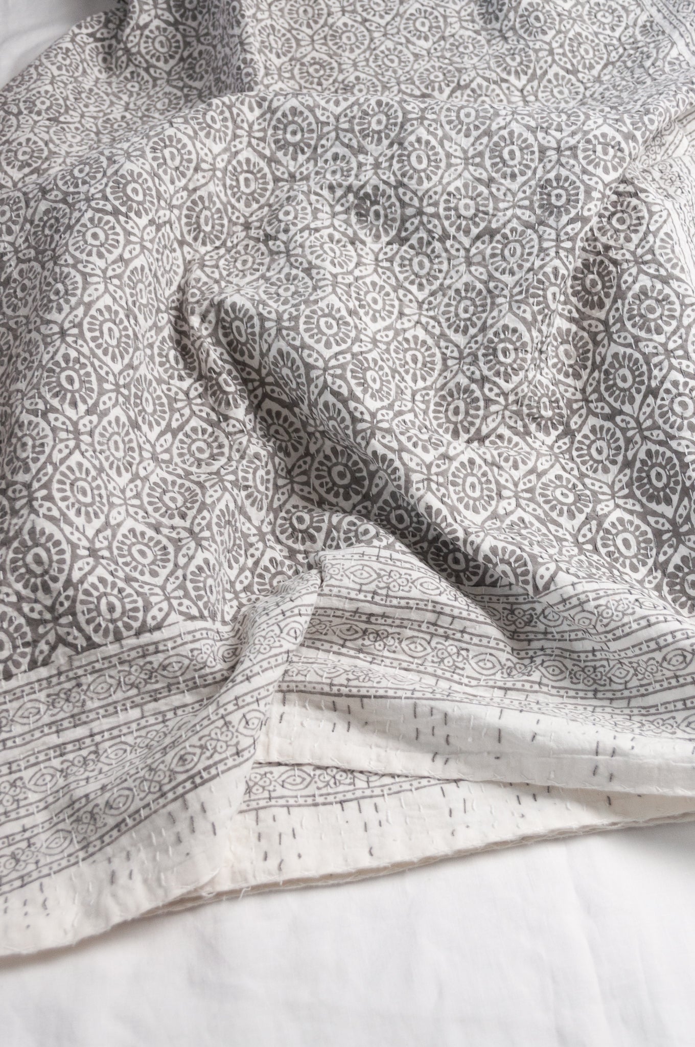 Cotton kantha quilt with an abstract floral design in silver grey on white.