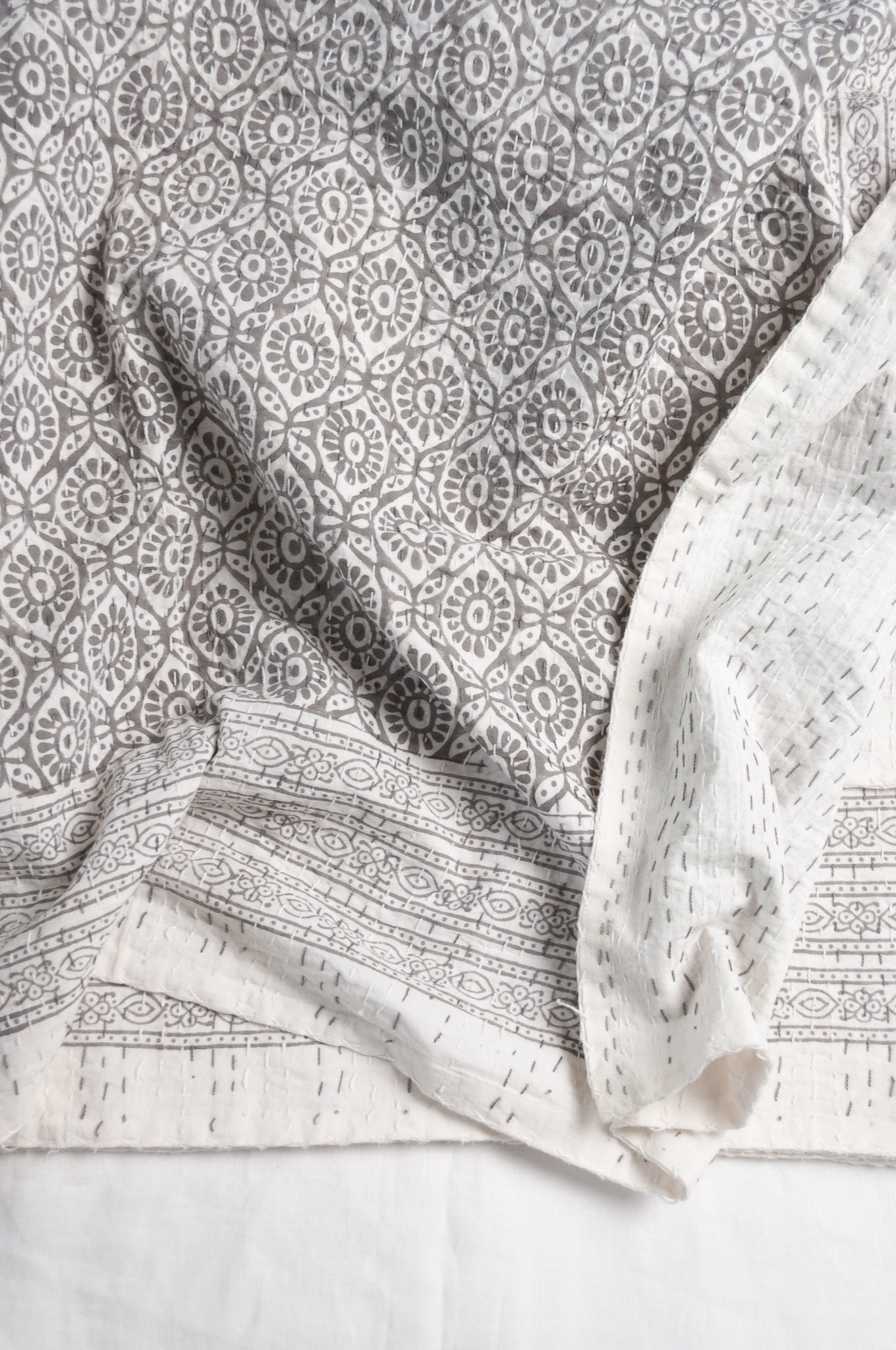 Cotton kantha quilt with an abstract floral design in silver grey on white.