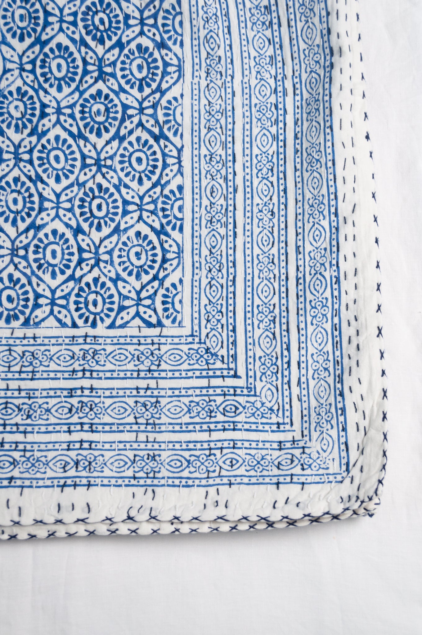 Cotton kantha quilt with an abstract floral design in blue on white.