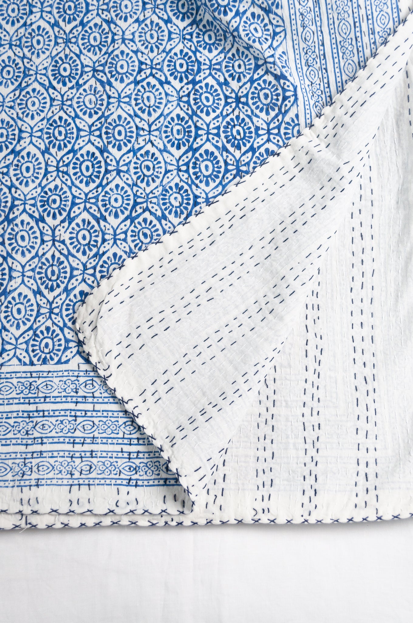 Cotton kantha quilt with an abstract floral design in blue on white.