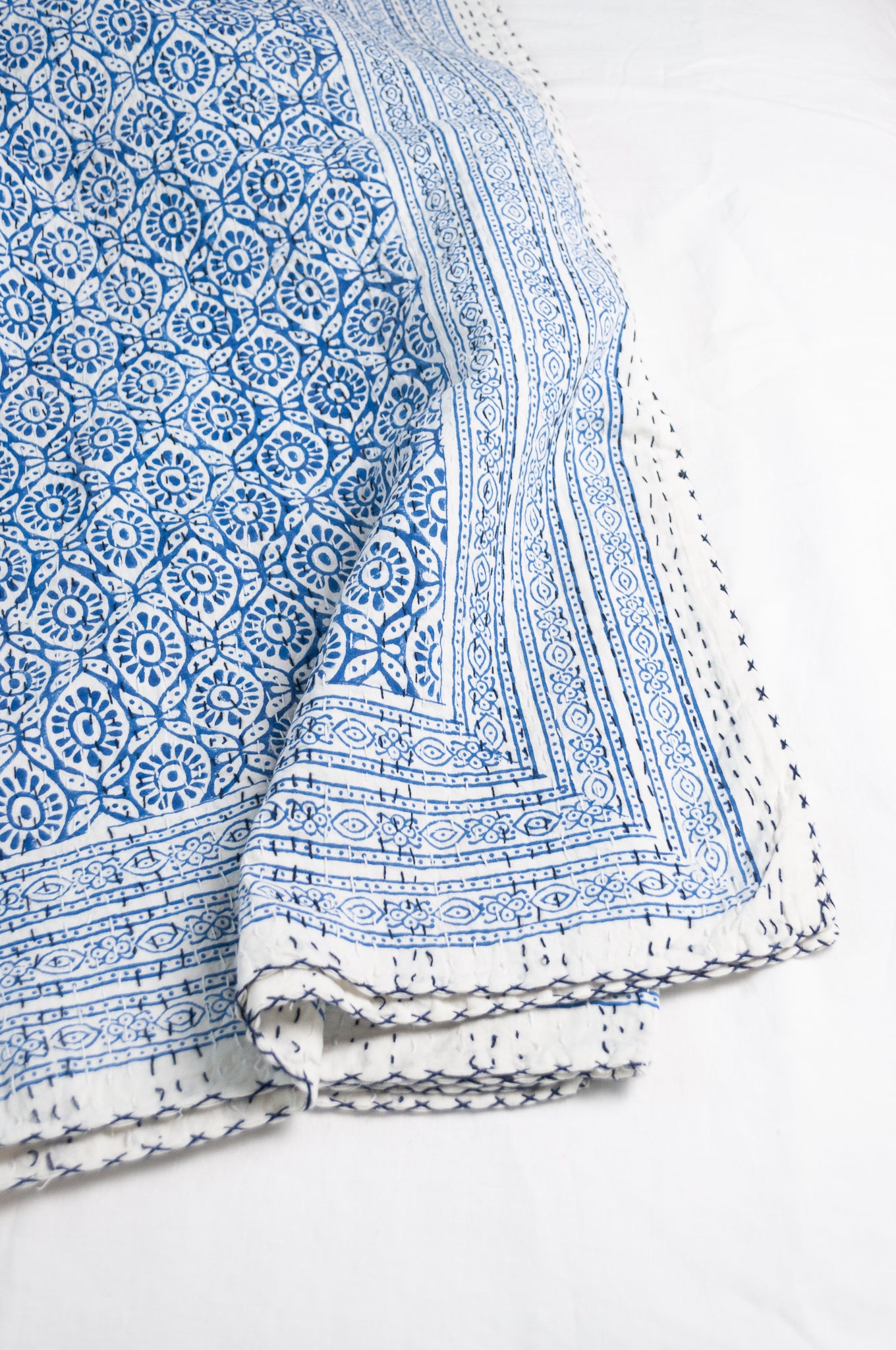 Cotton kantha quilt with an abstract floral design in blue on white.