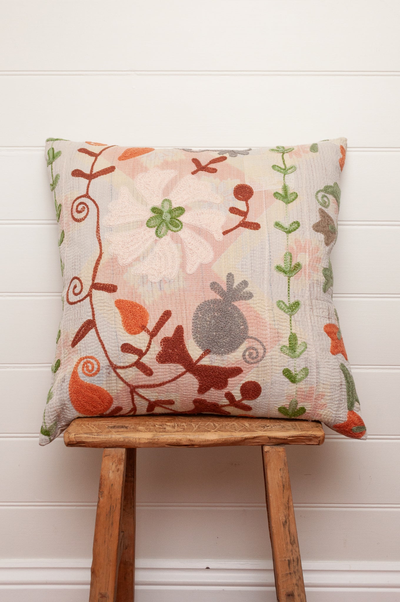Suzani embroidered vintage kantha cushion floral embroidery in rust, green, tan and grey on pastel pink background.