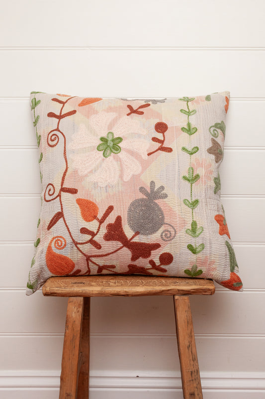 Suzani embroidered vintage kantha cushion floral embroidery in rust, green, tan and grey on pastel pink background.