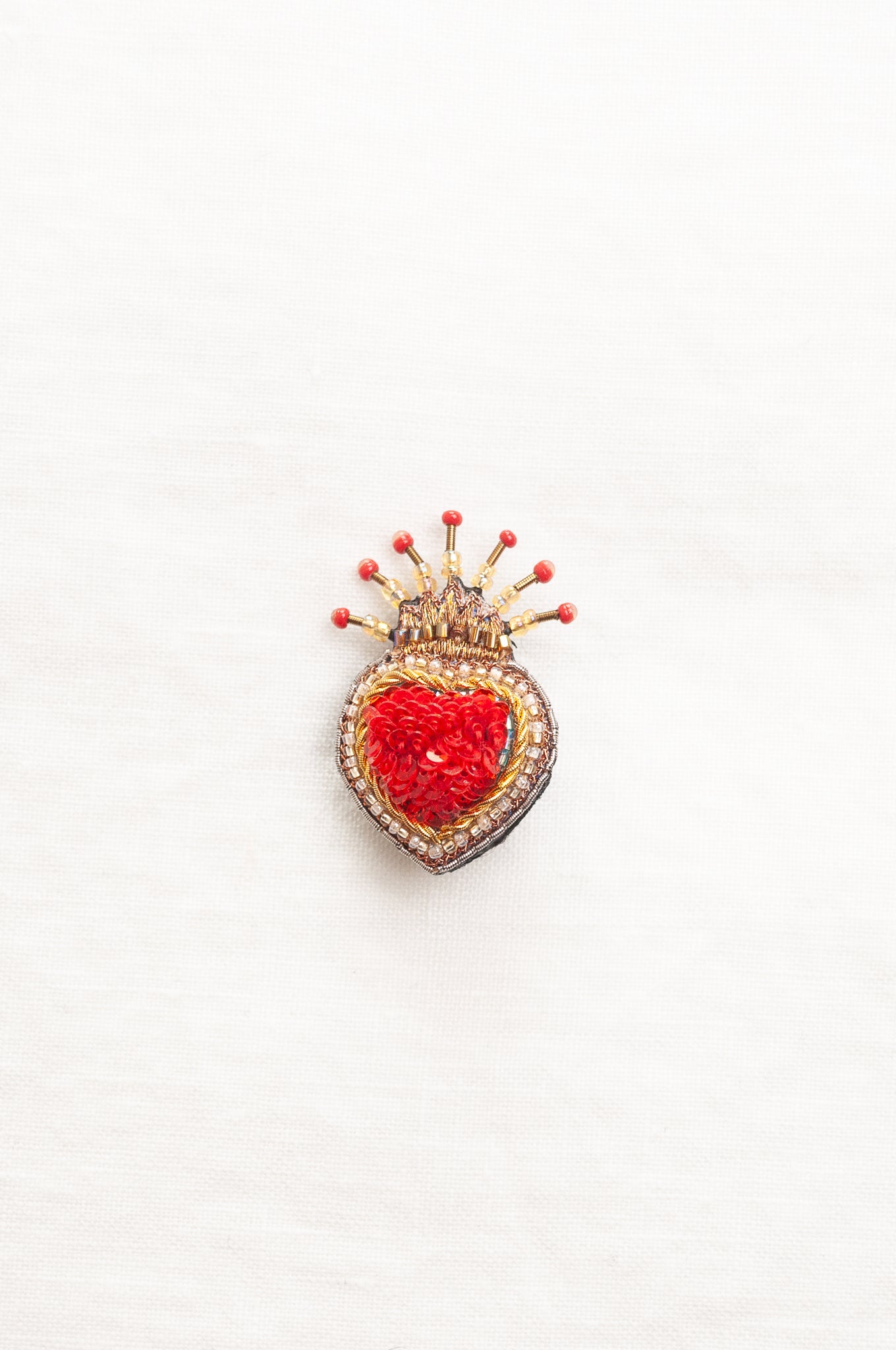 Trovelore Queen of Hearts hand beadedheart-shaped brooch featuring a vibrant red central heart, surrounded by a gold and silver beaded border, topped with a small gold crown adorned with red beads.