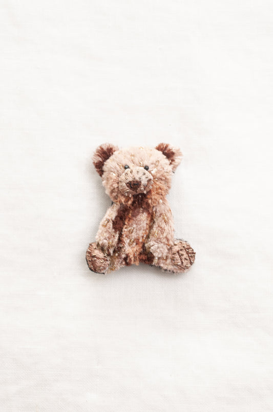 Trovelore hand crafted, and hand beaded small plush teddy bear brooch in mottled light brown and beige fabric.