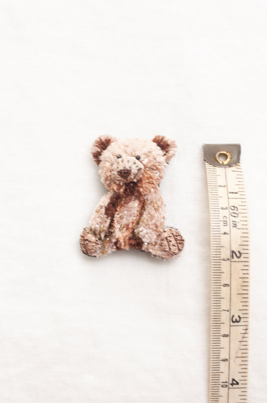 Trovelore hand crafted, and hand beaded small plush teddy bear brooch in mottled light brown and beige fabric.