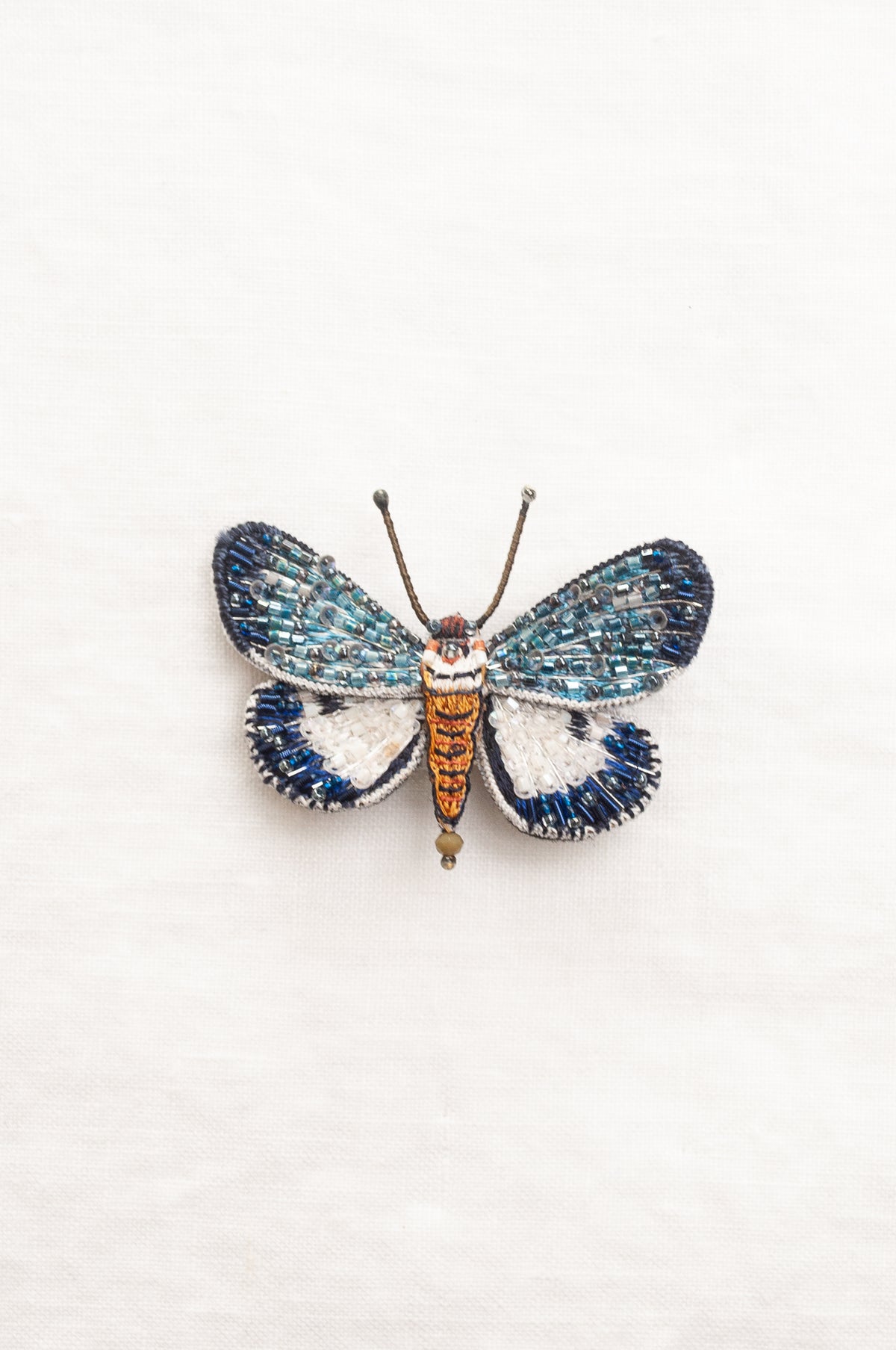 Trovelore Neochera moth hand beaded brooch, detailed butterfly-shaped brooch with iridescent blue and white wings, a metallic gold body, and delicate antennae.