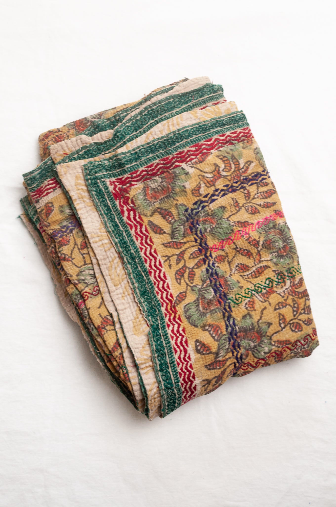 Vintage bagru blockprinted kantha quilt, floral design in rust red and sage green on a mustard yellow background, with red, blue and green traditional decorative embroidery