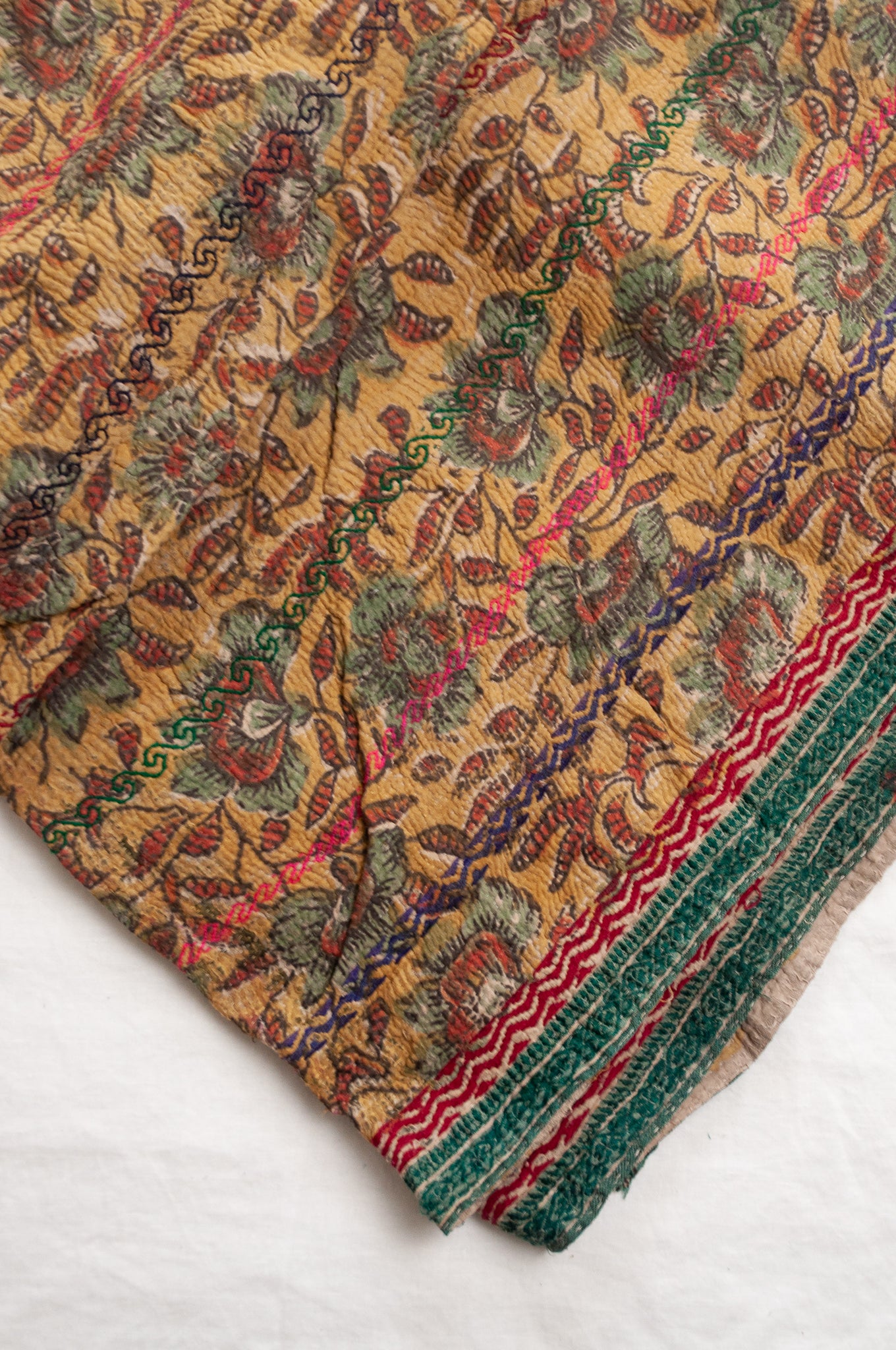 Vintage bagru blockprinted kantha quilt, floral design in rust red and sage green on a mustard yellow background, with red, blue and green traditional decorative embroidery