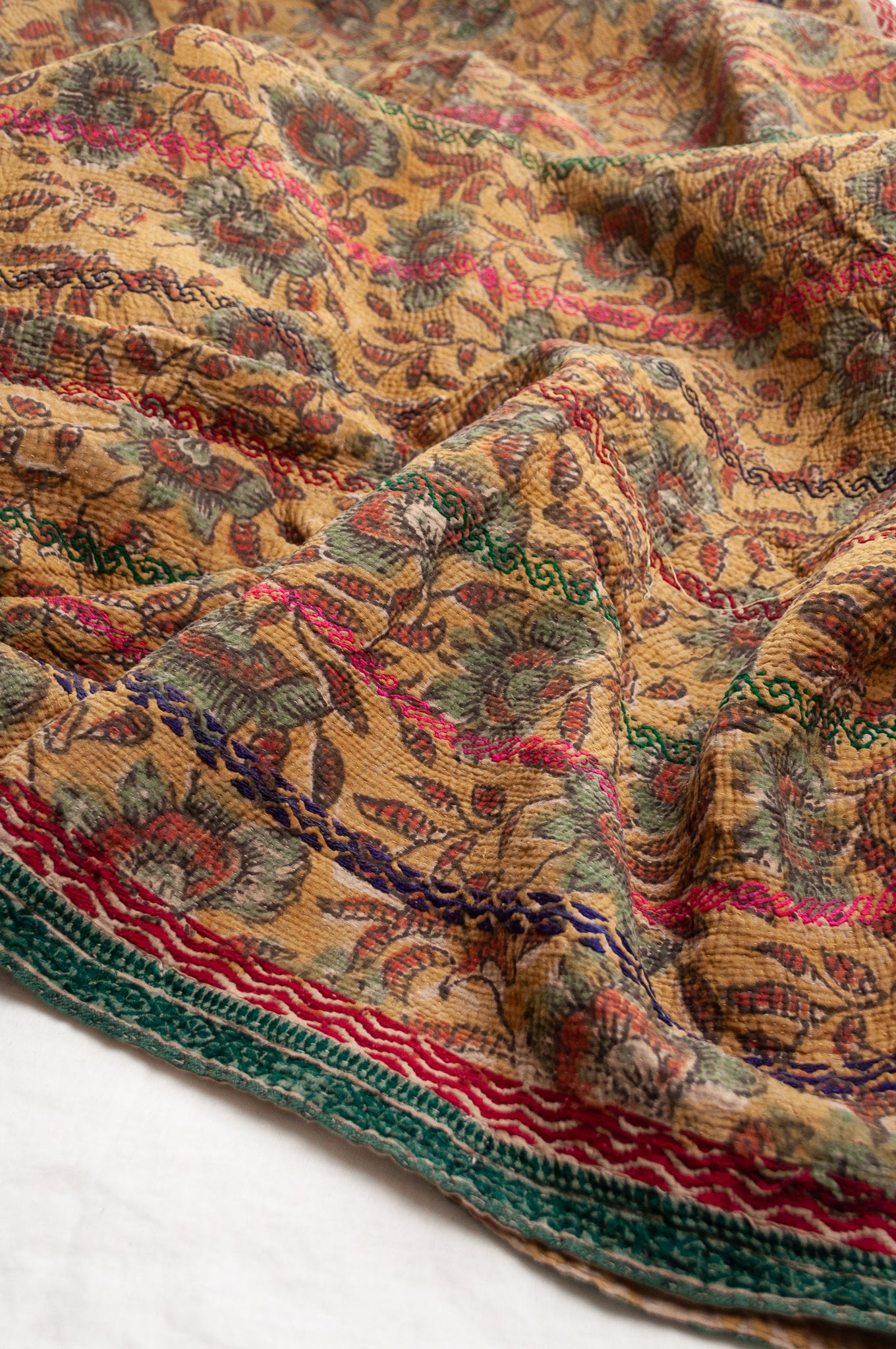 Vintage bagru blockprinted kantha quilt, floral design in rust red and sage green on a mustard yellow background, with red, blue and green traditional decorative embroidery