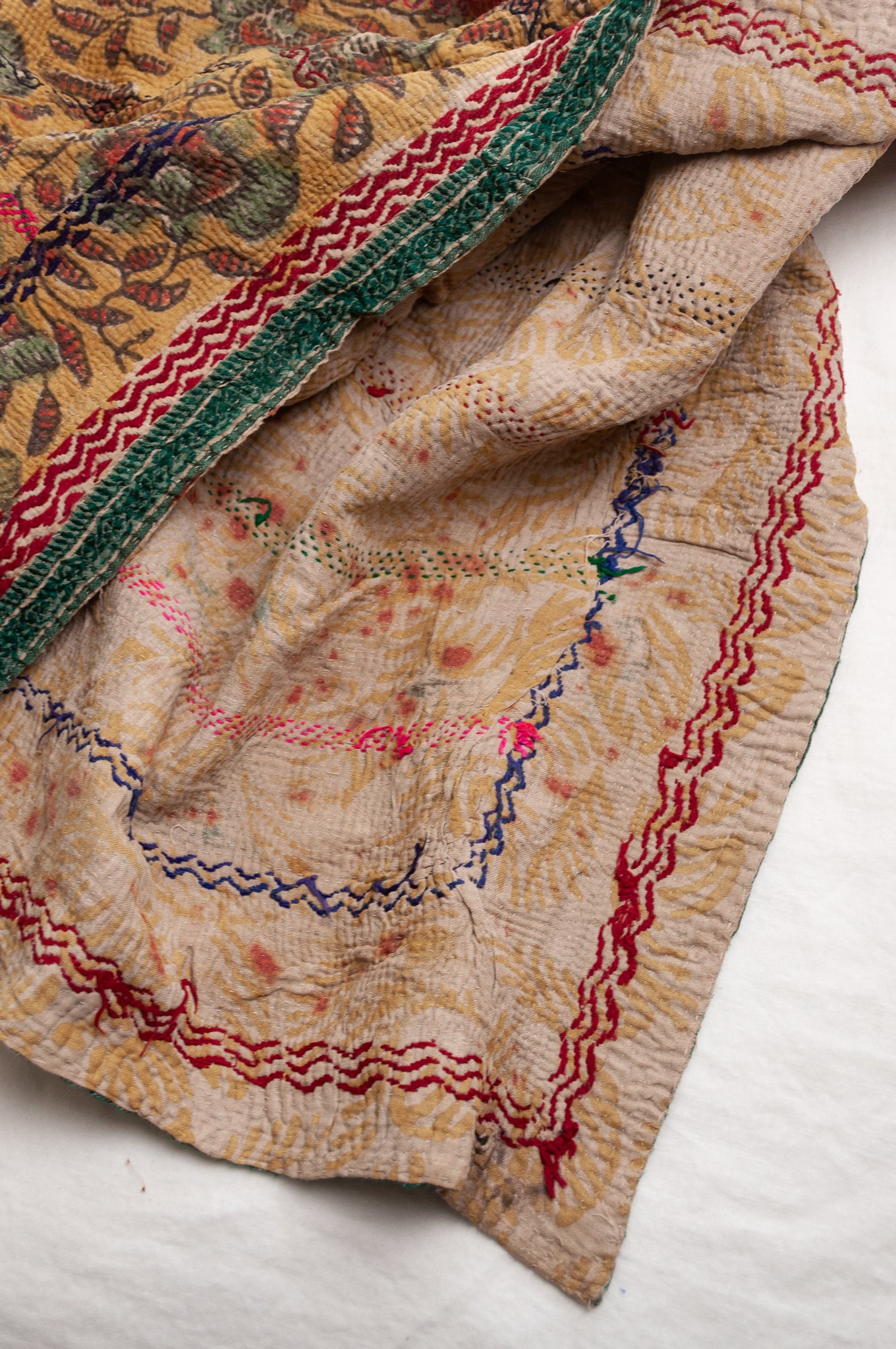 Vintage bagru blockprinted kantha quilt, floral design in rust red and sage green on a mustard yellow background, with red, blue and green traditional decorative embroidery