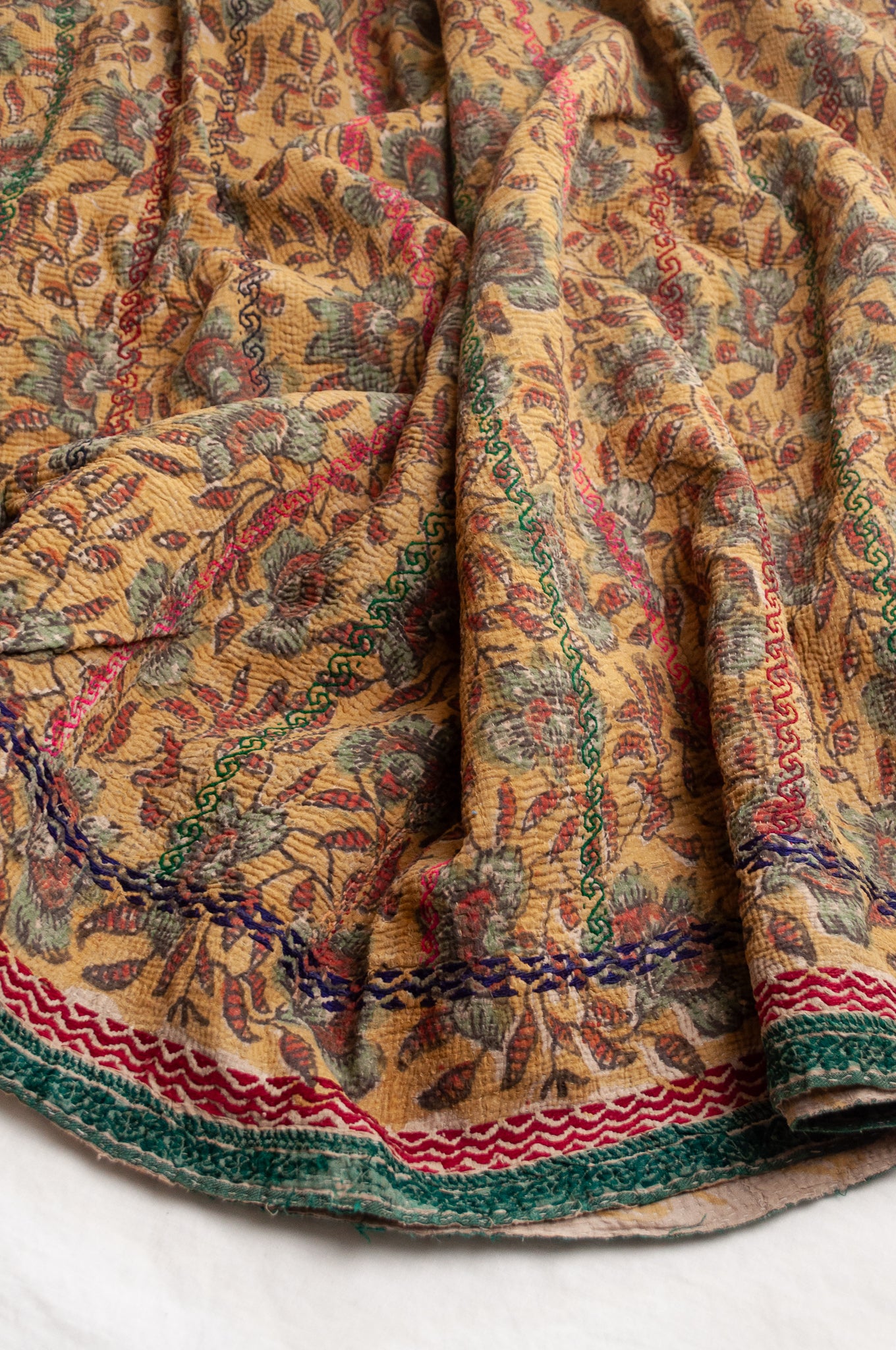 Vintage bagru blockprinted kantha quilt, floral design in rust red and sage green on a mustard yellow background, with red, blue and green traditional decorative embroidery