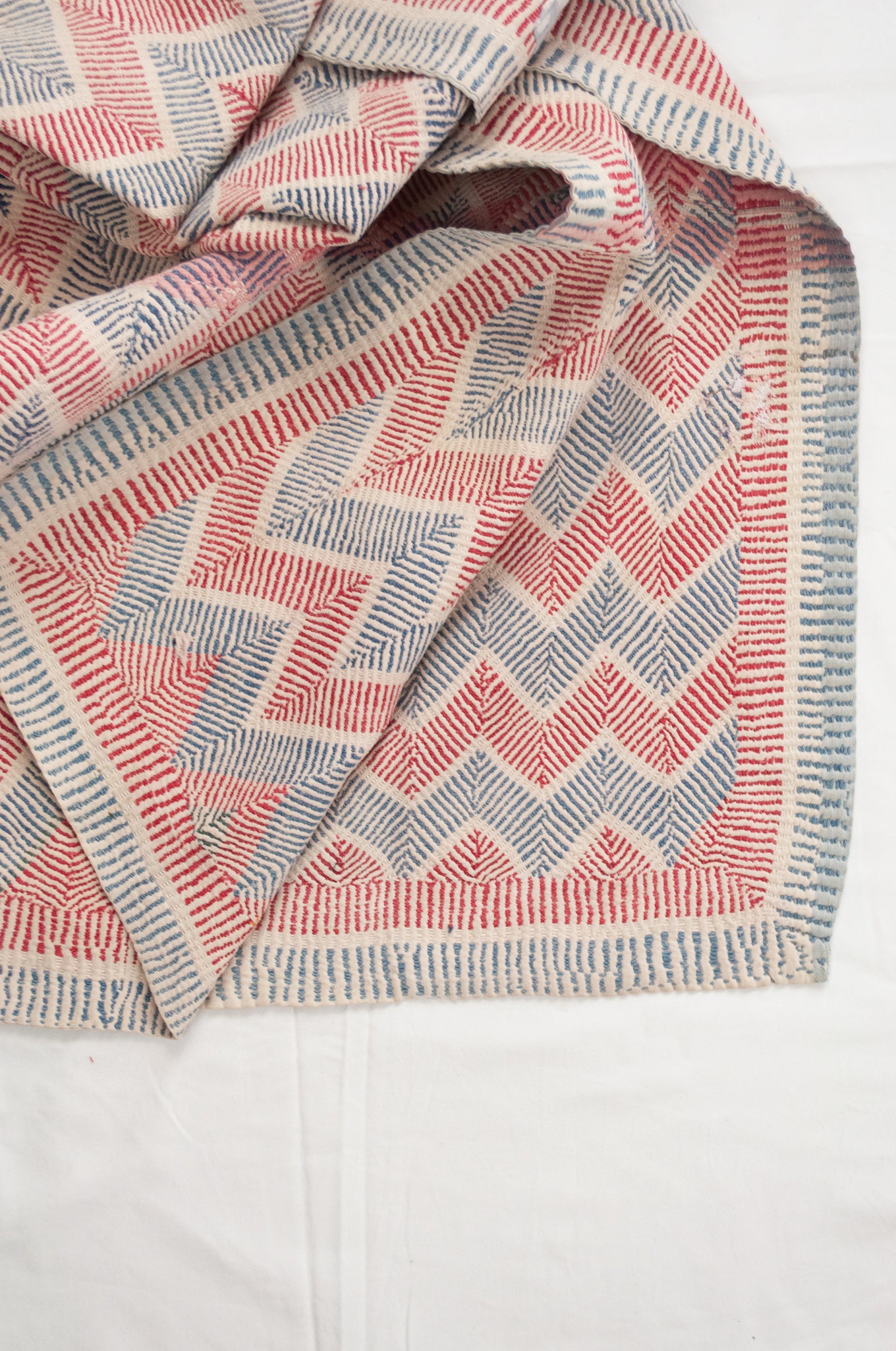 Traditional lohori wave kantha quilt red and blue stitching on white background.