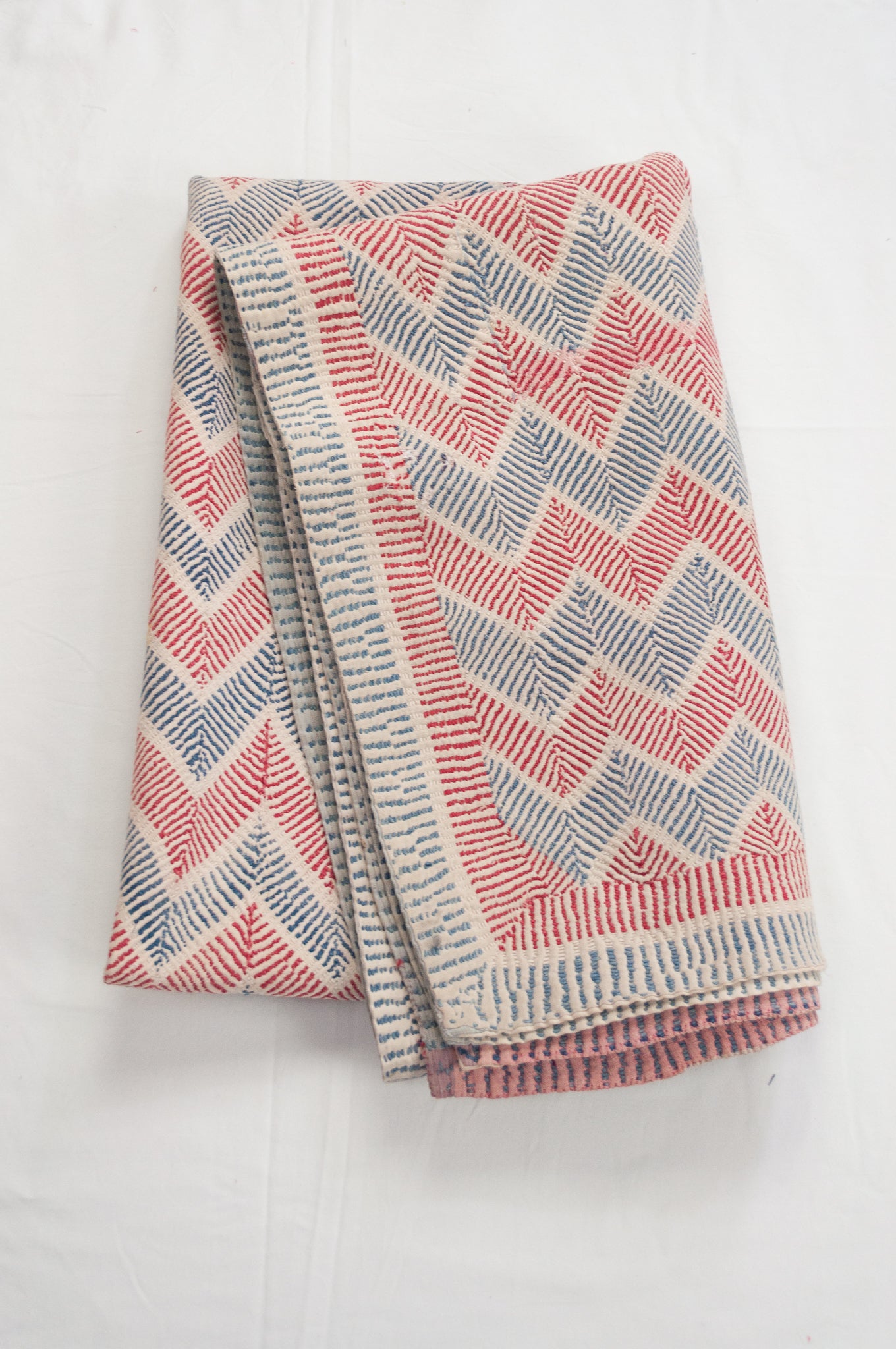 Traditional lohori wave kantha quilt red and blue stitching on white background.