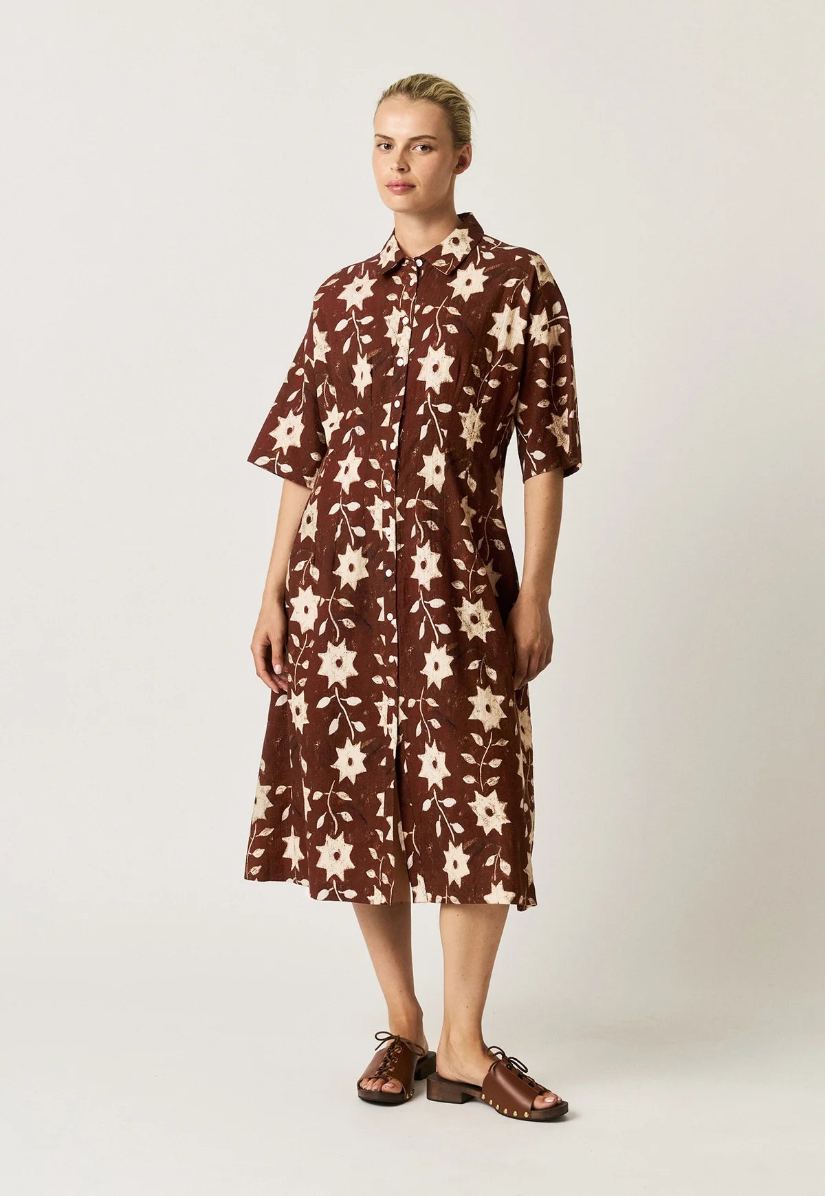 Nancybird Paloma short-sleeved button-front dress with an allover floral and starburst pattern in cream on a dark reddish-brown background.