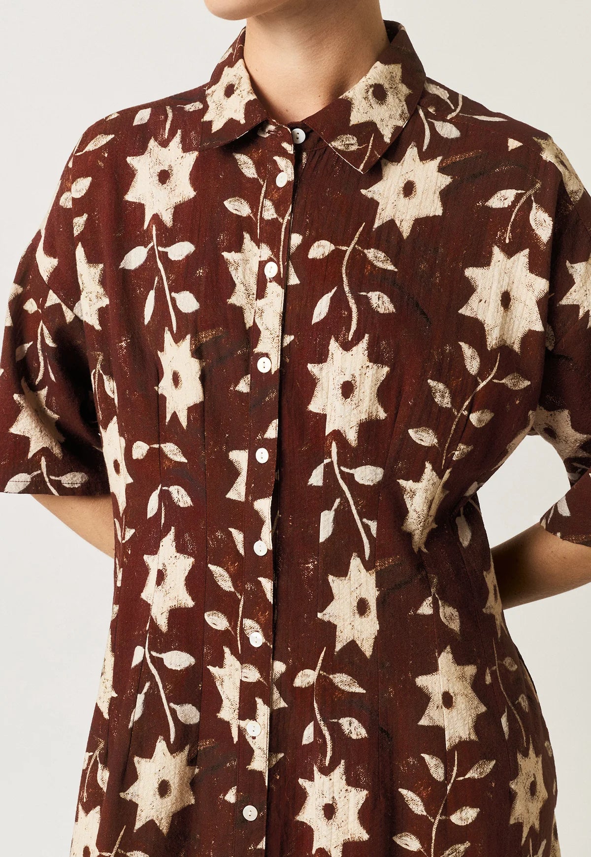 Nancybird Paloma short-sleeved button-front dress with an allover floral and starburst pattern in cream on a dark reddish-brown background.