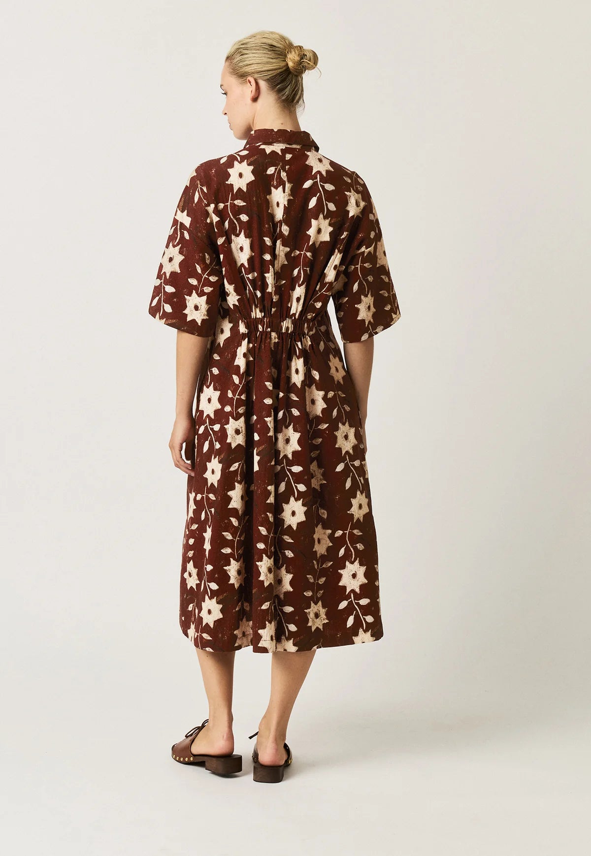 Nancybird Paloma short-sleeved button-front dress with an allover floral and starburst pattern in cream on a dark reddish-brown background.