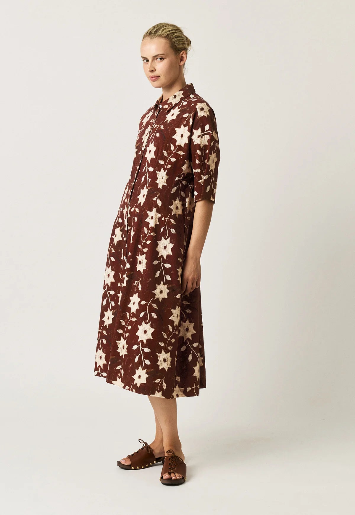 Nancybird Paloma short-sleeved button-front dress with an allover floral and starburst pattern in cream on a dark reddish-brown background.