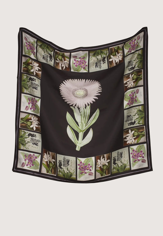 A square silk scarf featuring a central black field with a large pale pink and green flower, surrounded by a border of small botanical illustrations, Nancybird charcoal archive floral print.