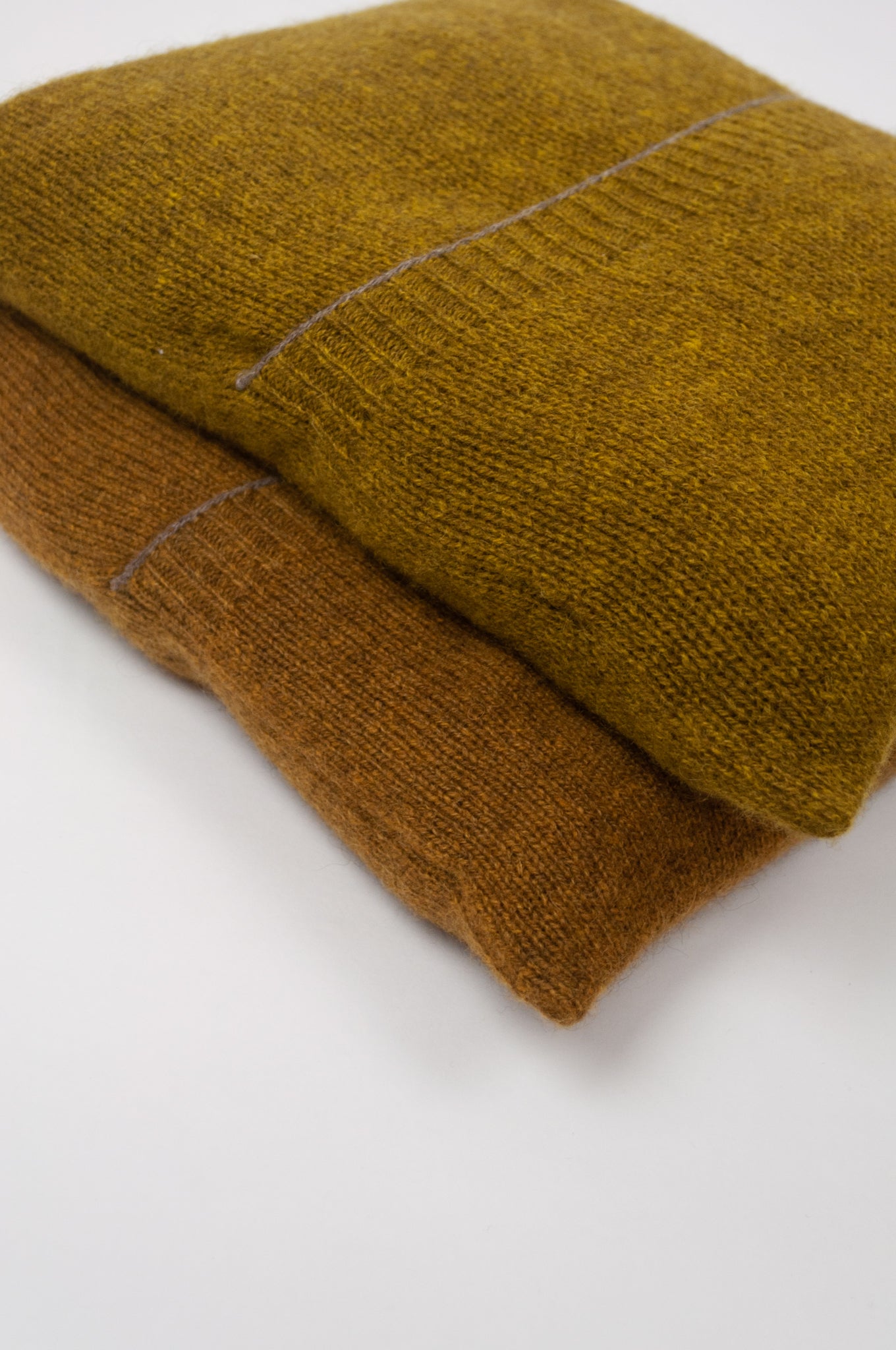 Juniper Hearth baby yak wool poncho in Weed, a deep yellow olive green shade and also in Maize (bottom). Close up, in pouches.