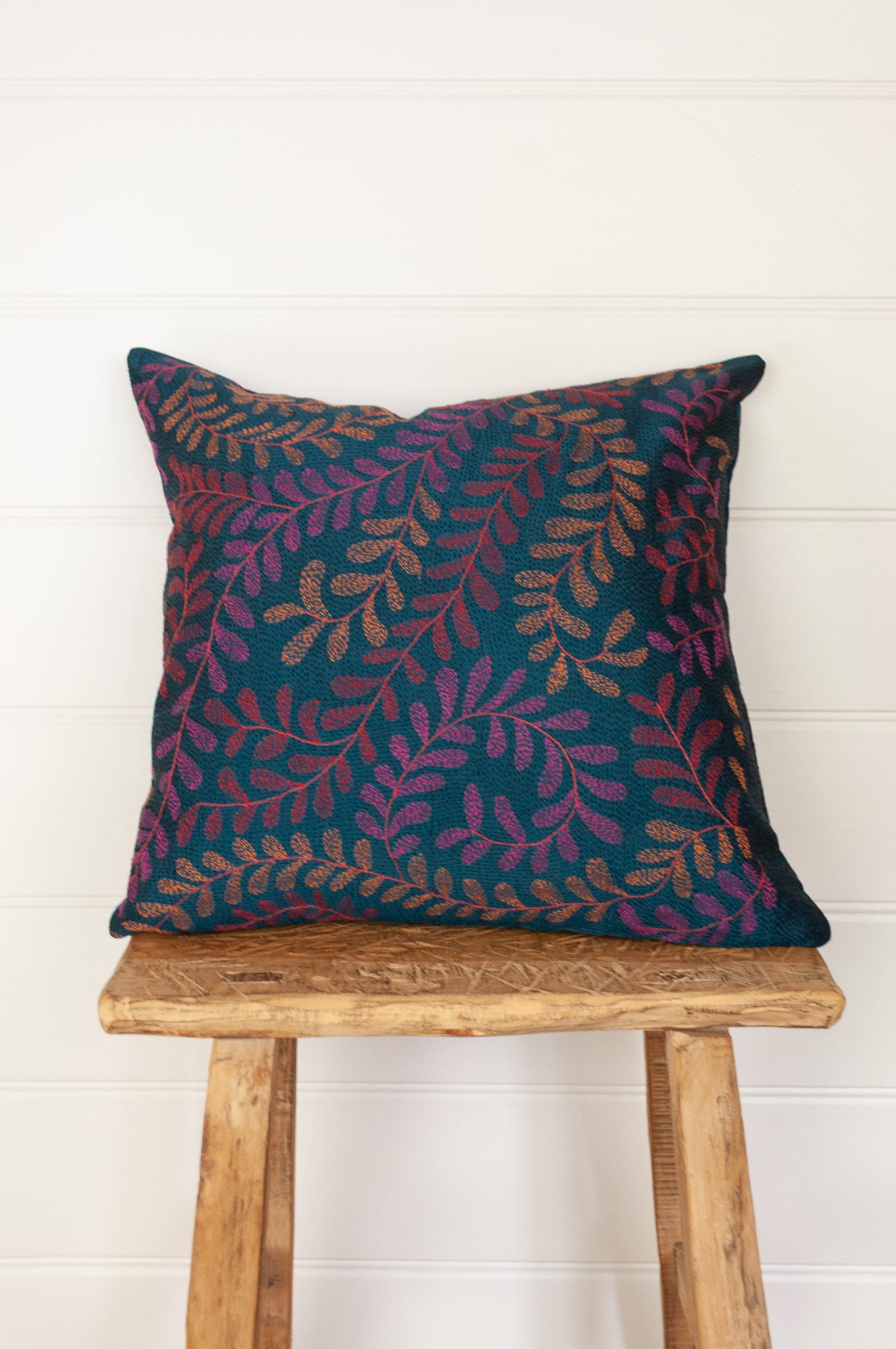 Kantha stitched on vintage silk, this square cushion features an allover tracery of vine leaves in cherry red, rose pink and apricot on a black stitched teal blue background